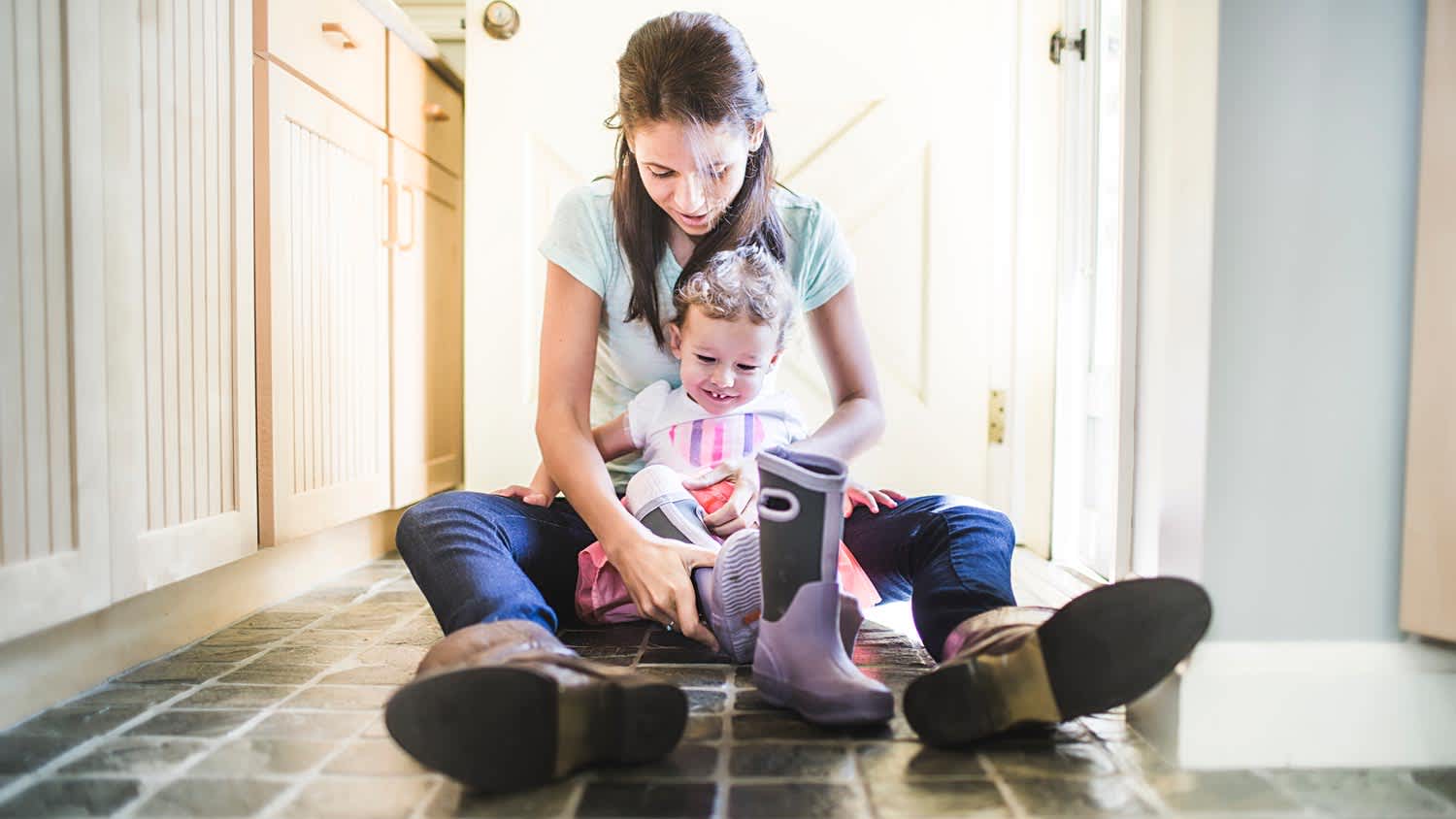 A mother and her daughter putting shoes on the kitchen tile floor