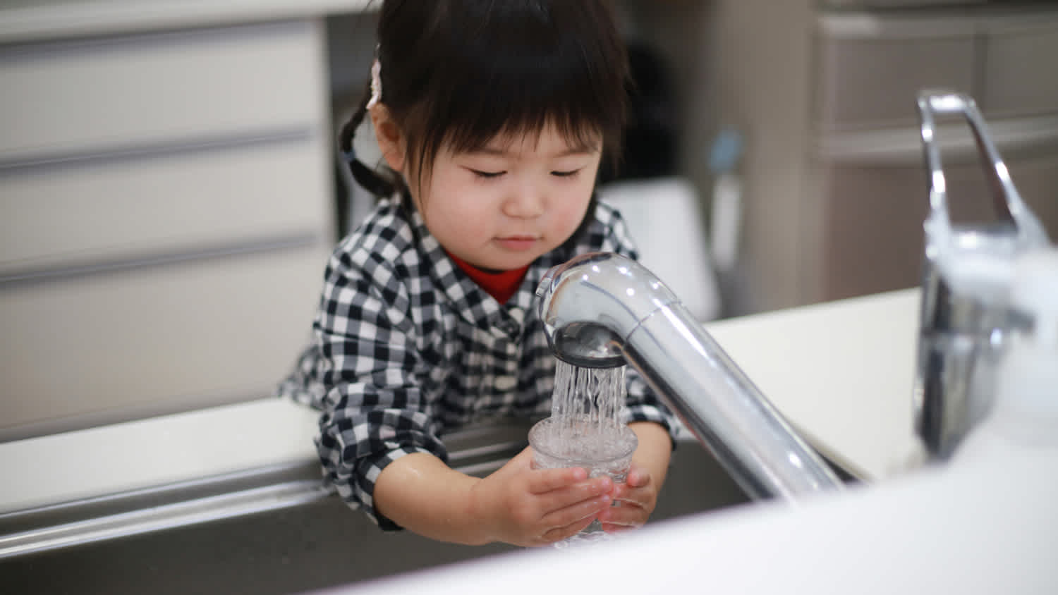 A kid filling a glass with tap water