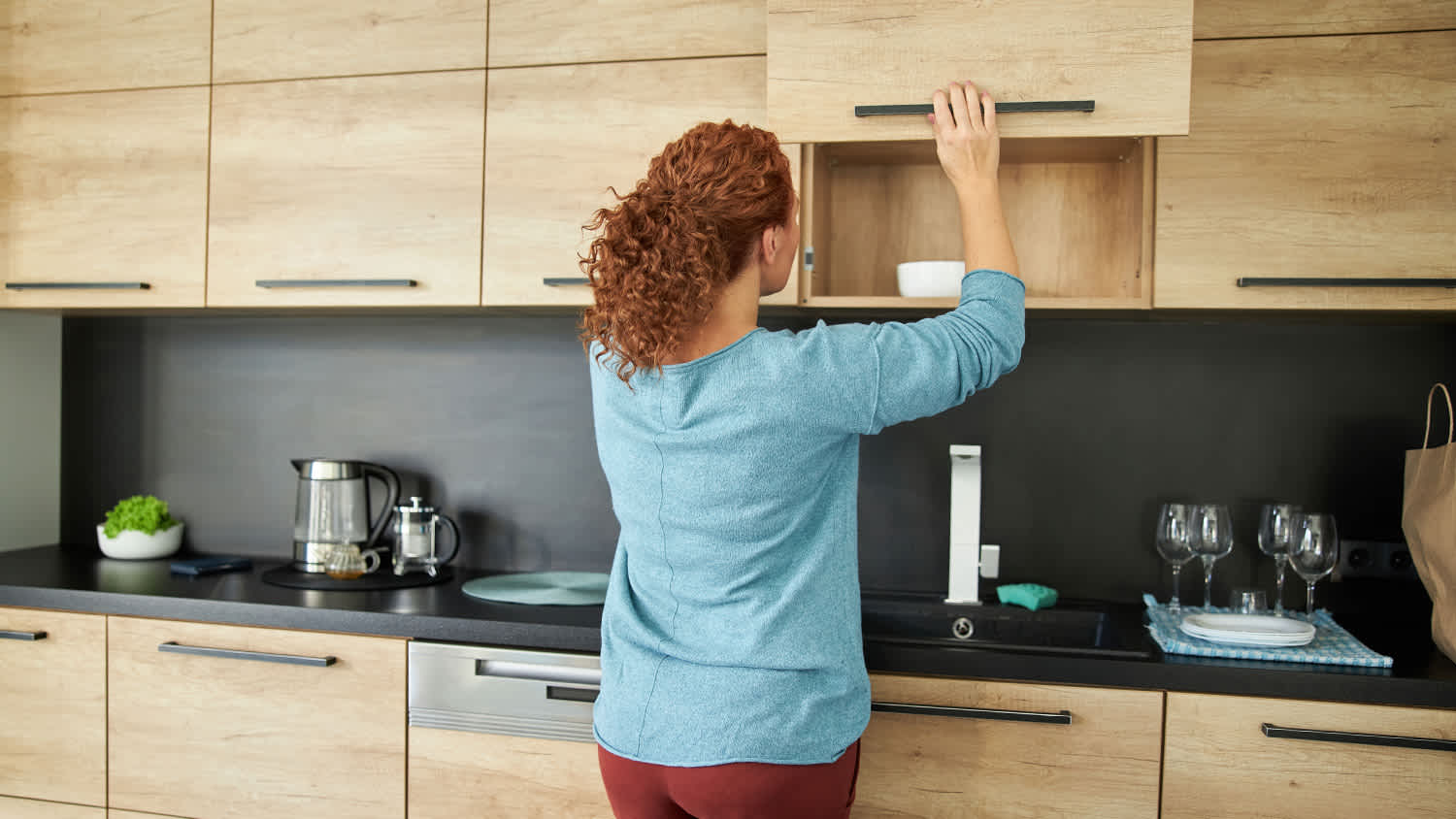 woman in kitchen opening brown cabinets