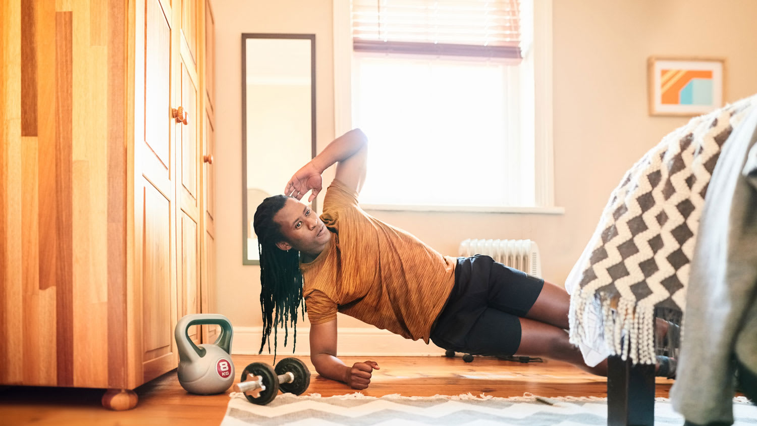 A man working out in his bedroom with dumbbells next to him