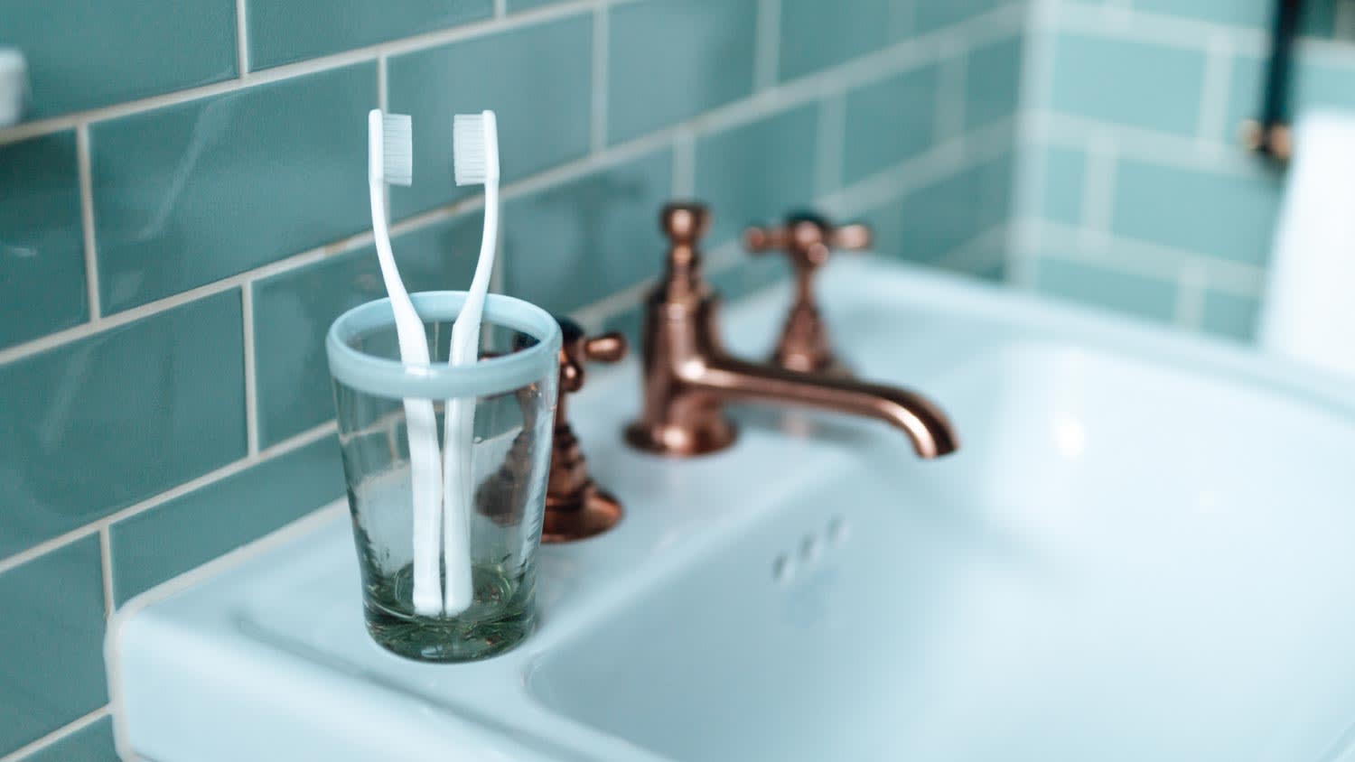 Two toothbrushes in cup sitting on bathroom sink