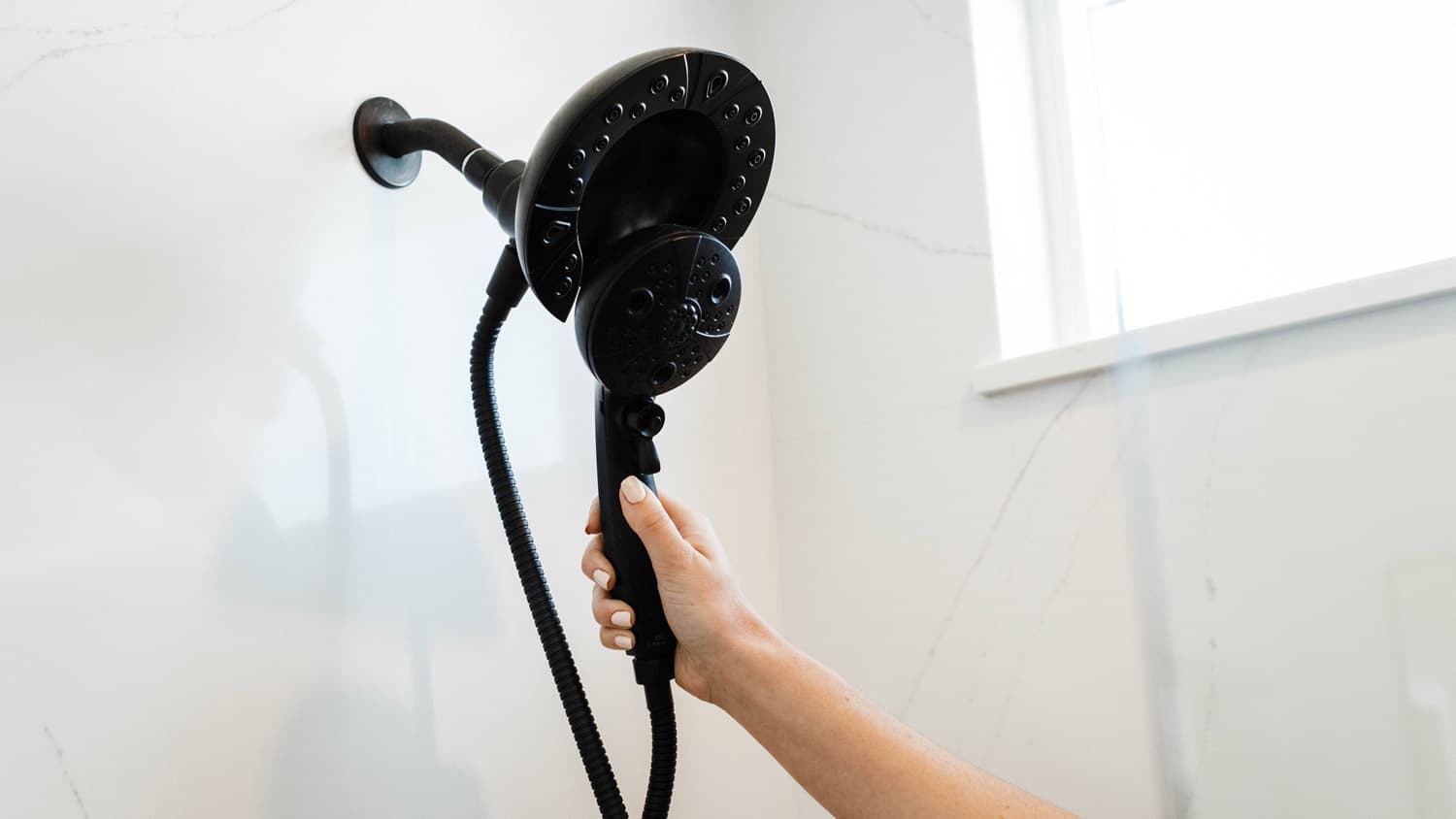 A woman’s hand holding a black shower head