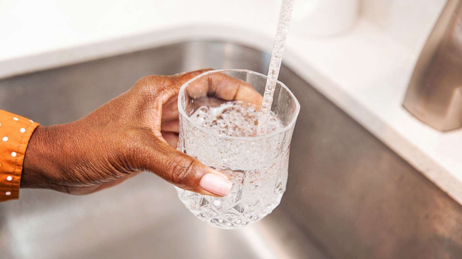 Close-up of woman’s hand holding a glass under the tap