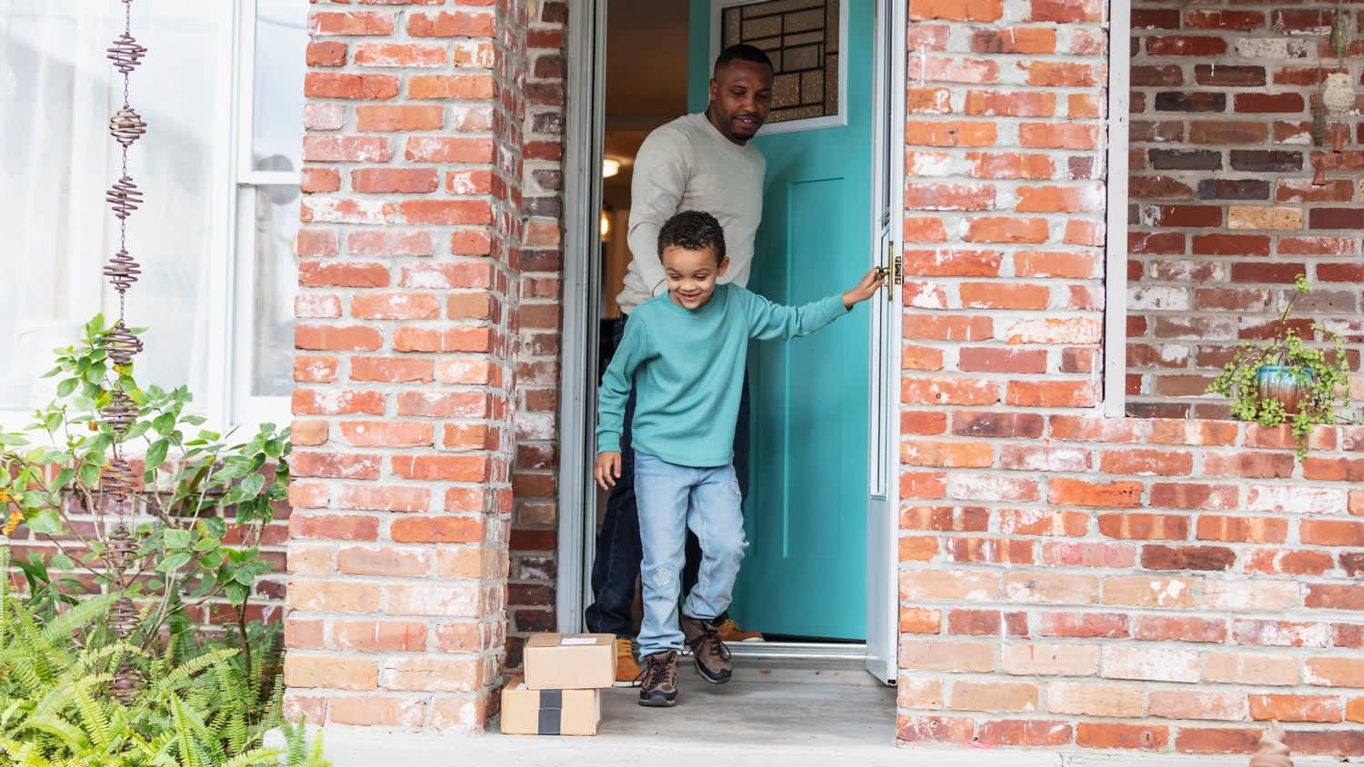 A father and his son exiting a brick house