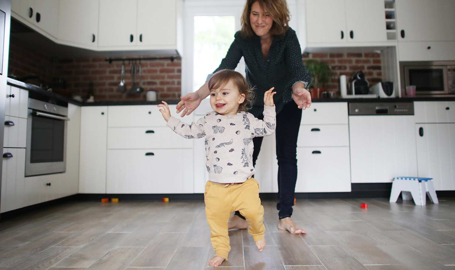 Mom chases baby across tile floor in kitchen
