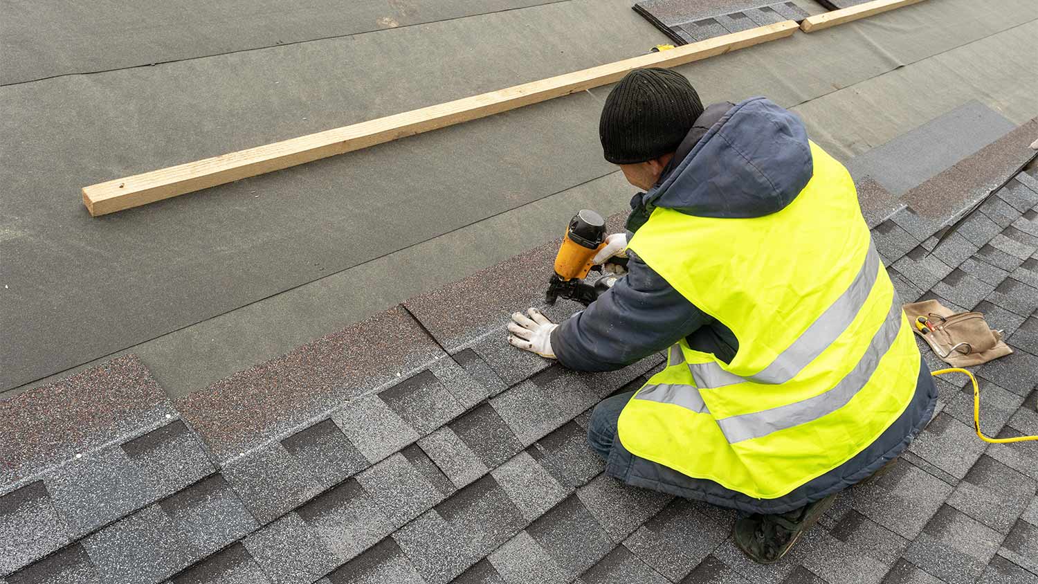 man installing asphalt shingles on roof of home
