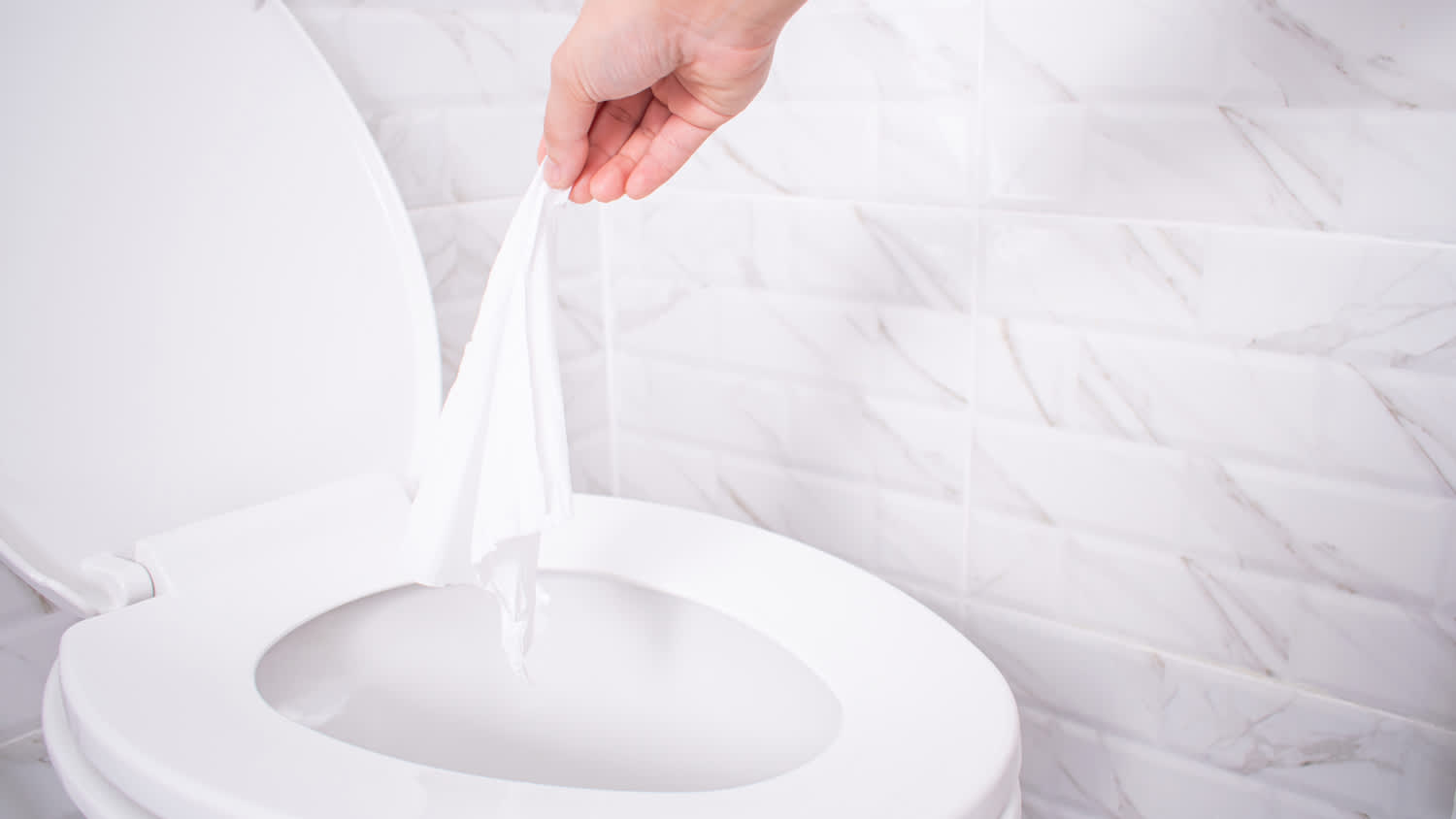 A hand throwing a flushable wipe in the toilet