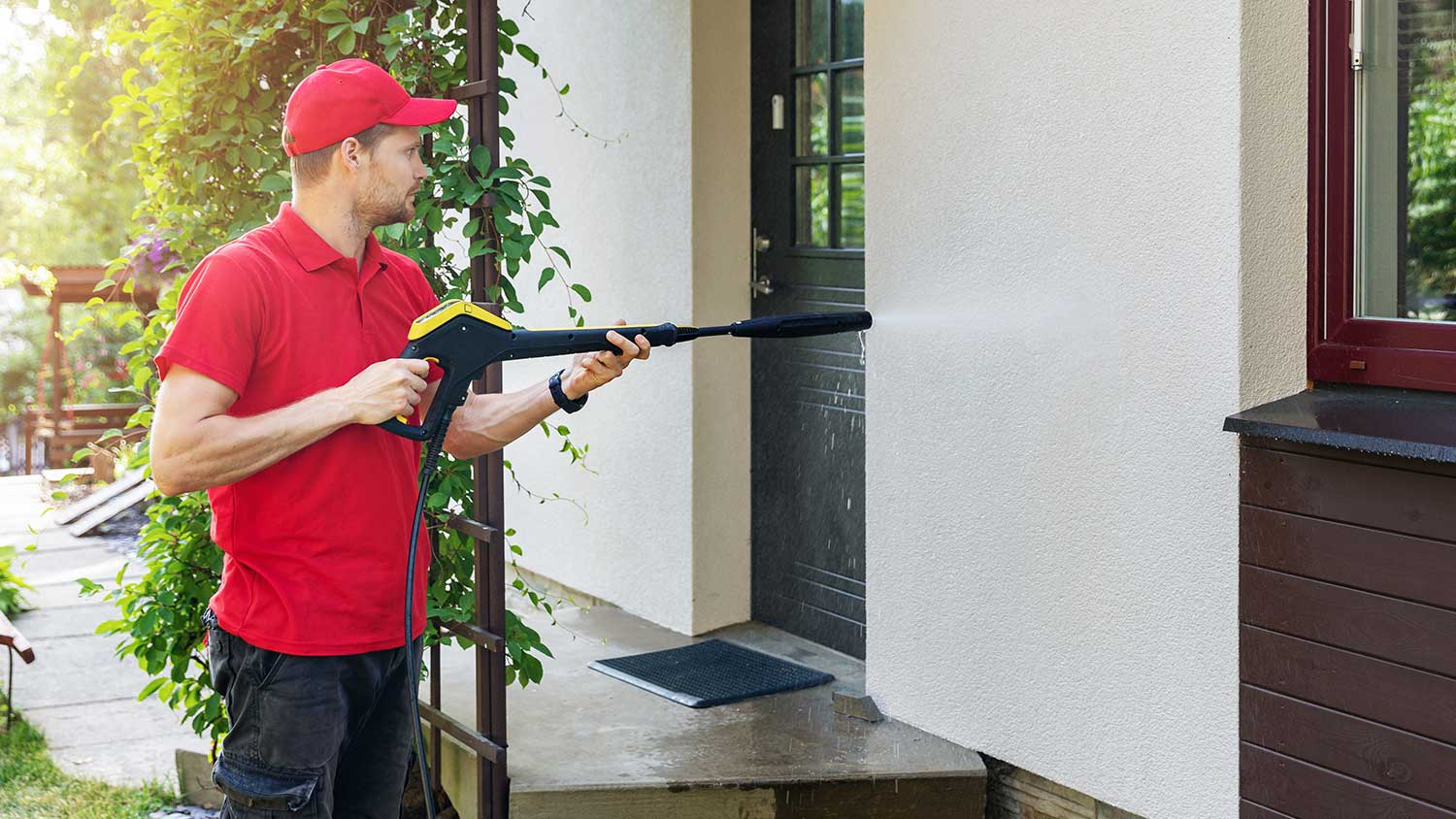 Man using pressure washer to clean exterior wall