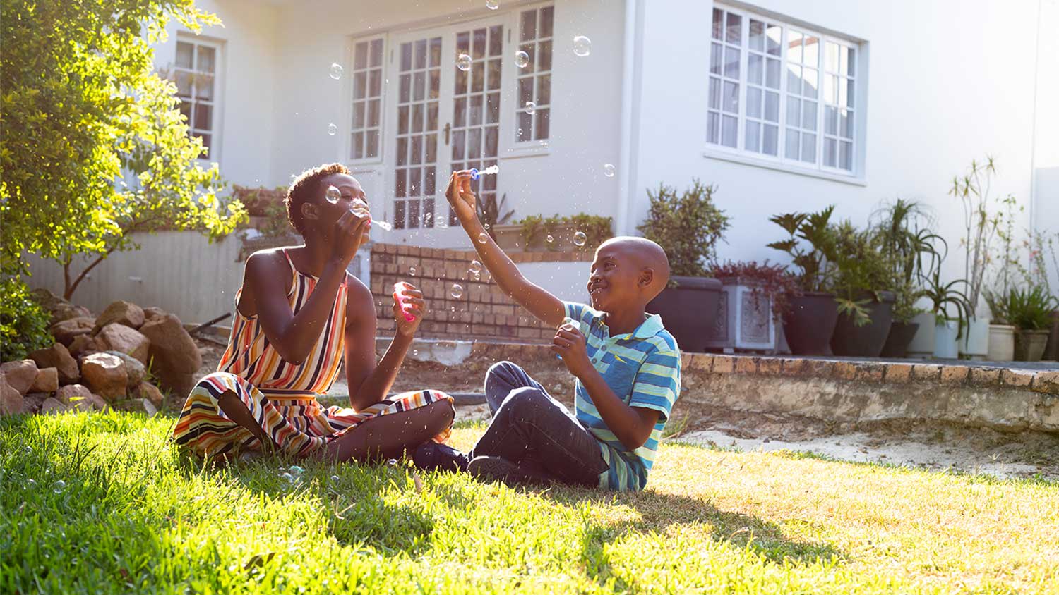 A mother and son blow bubbles in a backyard
