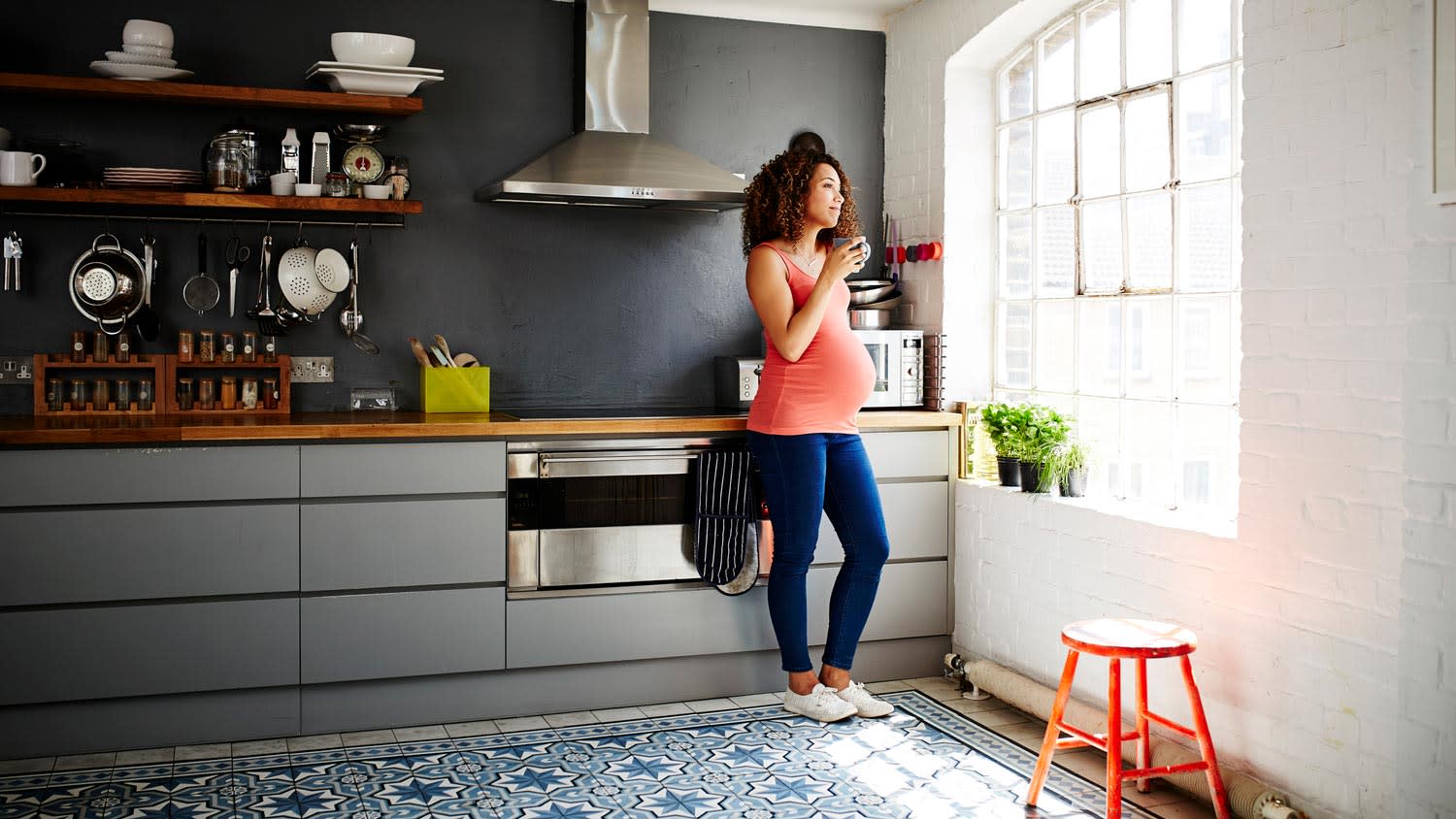 A pregnant woman drinking coffee in her dark gray painted kitchen