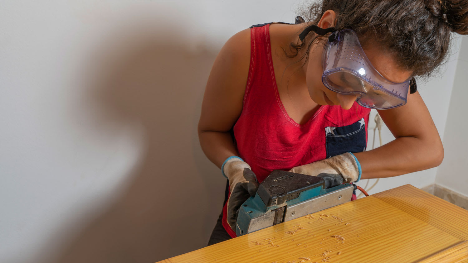 A woman with protective glasses planing a door