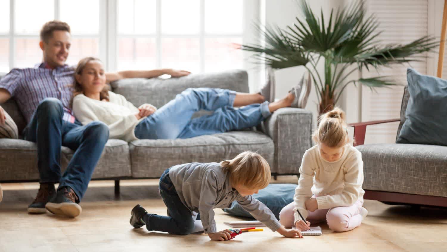 Children playing together on floor while parents relaxing at home