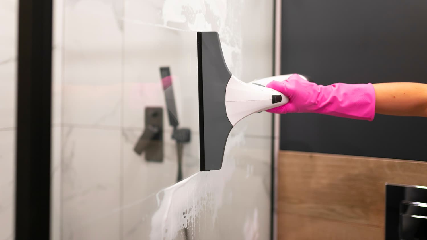 A woman in protective gloves cleaning a shower door