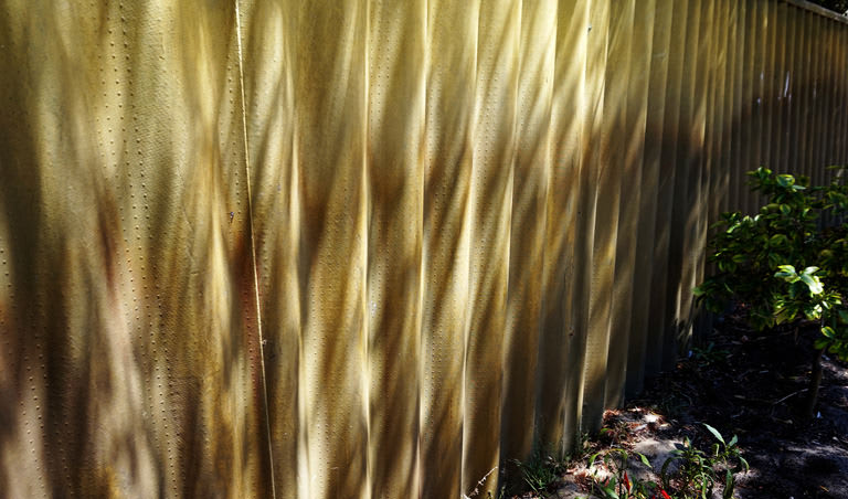 A sunlit corrugated fence in a garden
