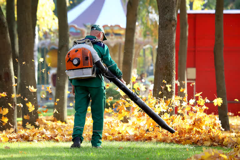 man with leaf blower blowing fall leaves into pile