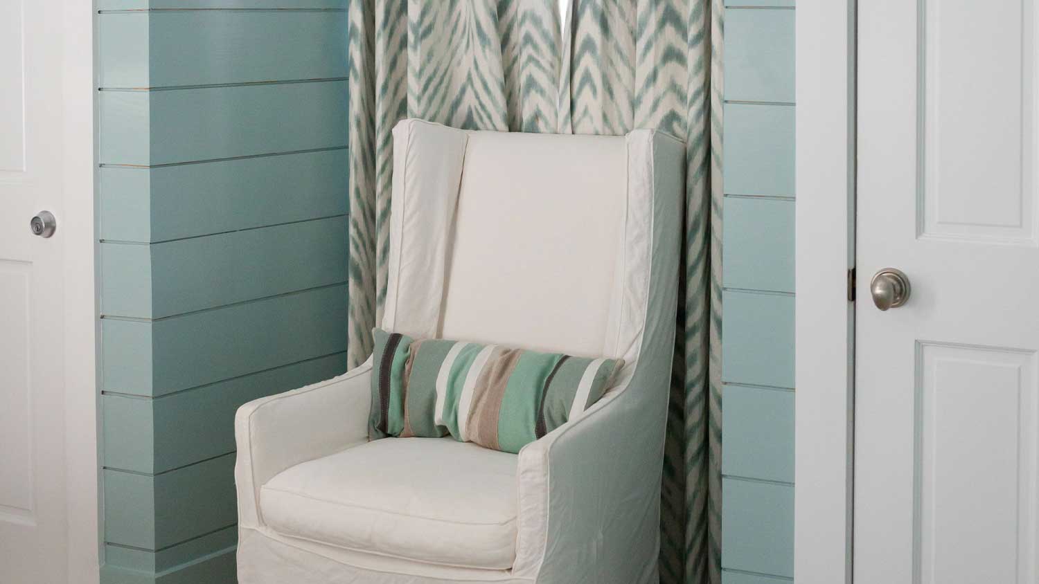 Bedroom with blue shiplap walls and a white armchair in an alcove