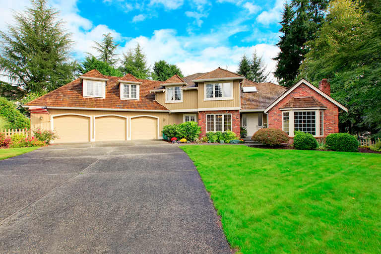 asphalt driveway leading to large home with triple garage doors and green grass