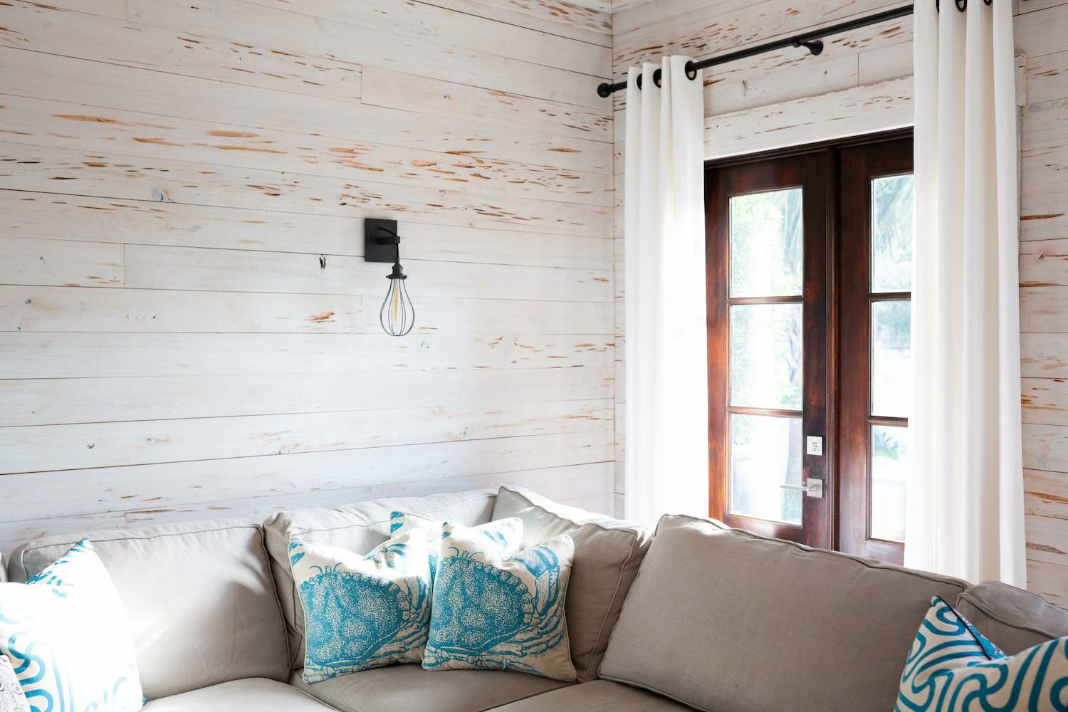 Beach-themed living room with gray couch, nautical throw pillows and white weathered shiplap walls