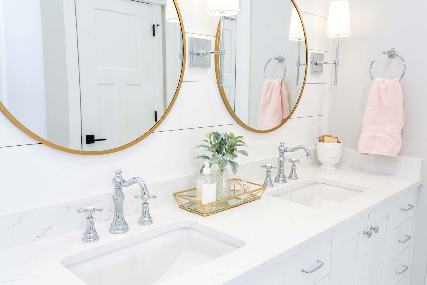 White bathroom vanity in front of white shiplap bathroom accent wall with two gold circle mirrors