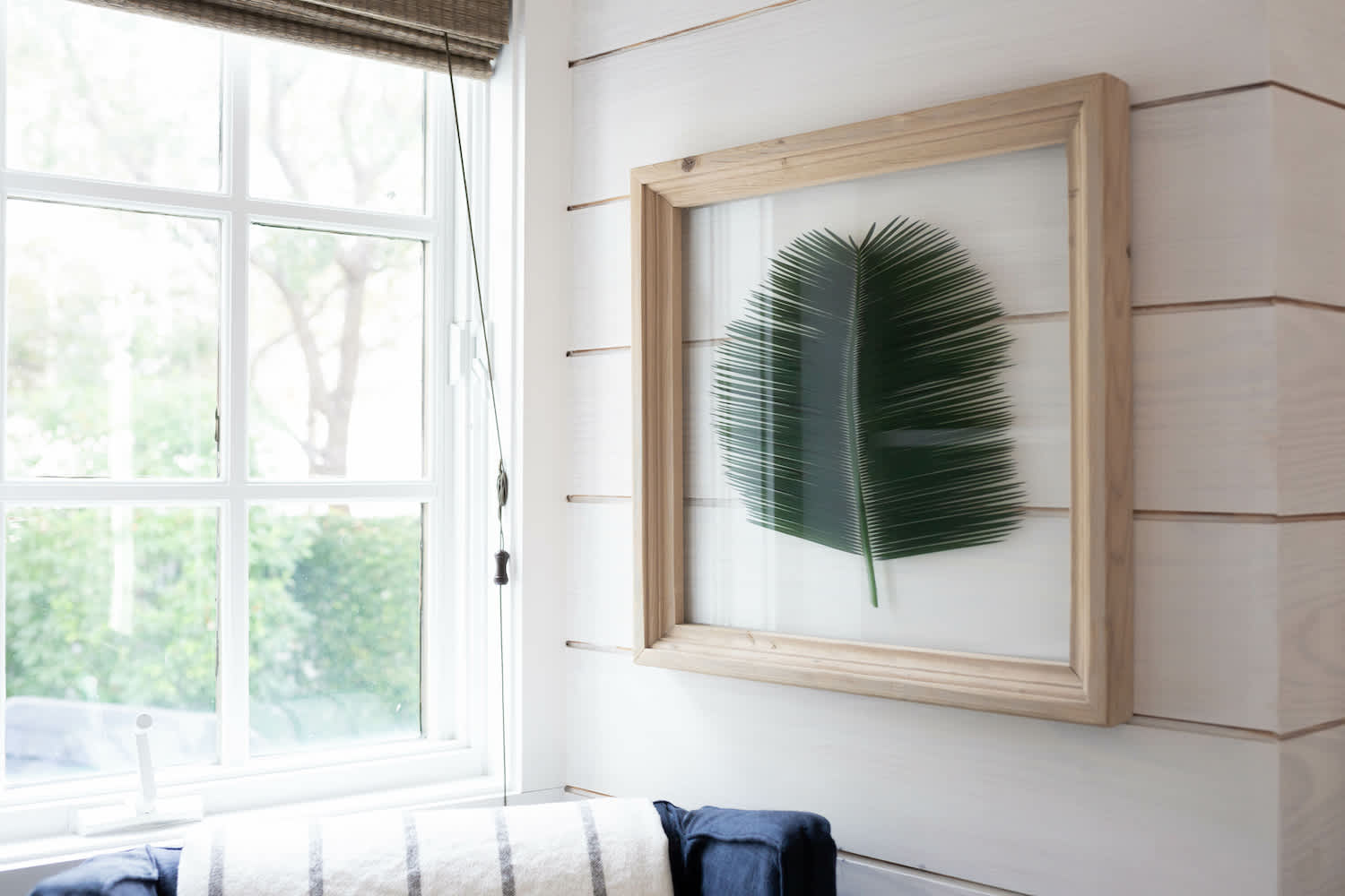 Shiplap accent wall with framed palm leaf next to open window and navy chair