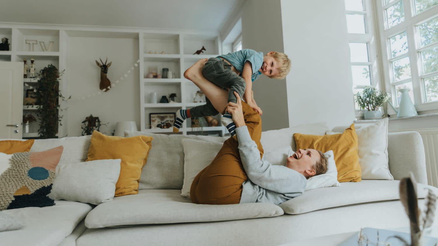 Mother picking son on leg while playing on sofa at home