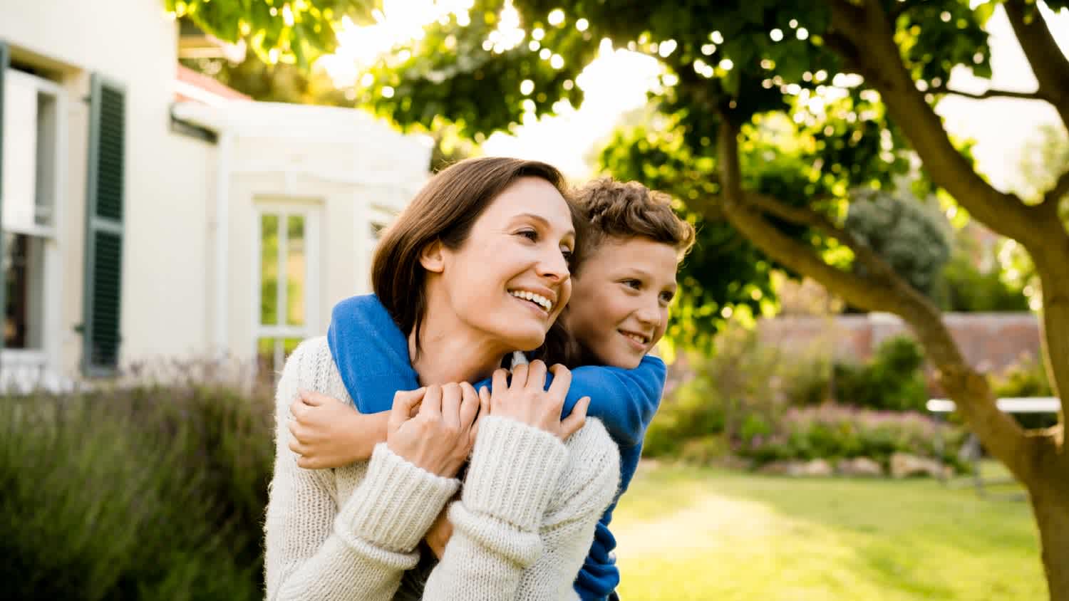 A boy embracing mother outside house