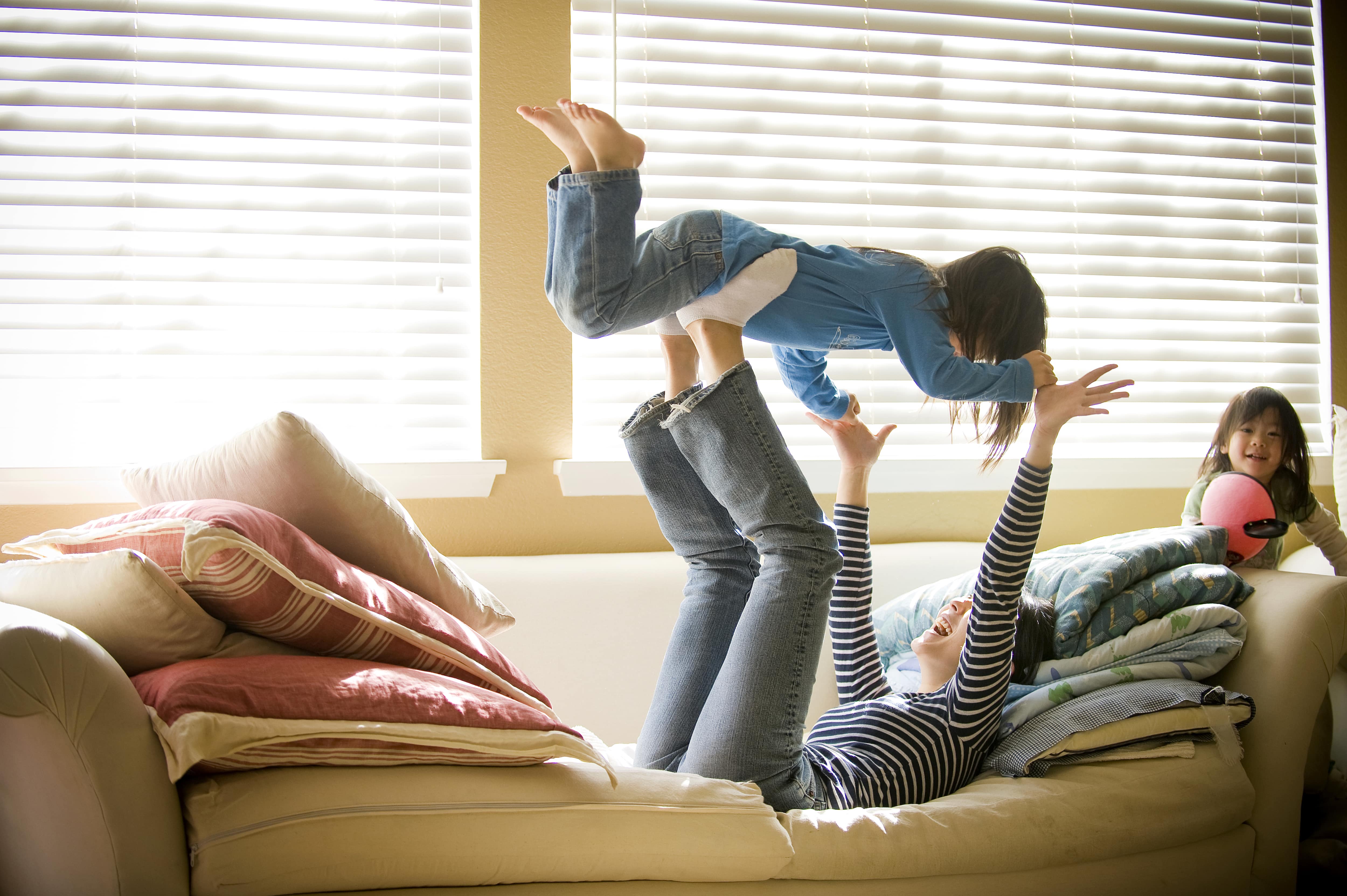 Mother playing with daughters in front of window with blinds