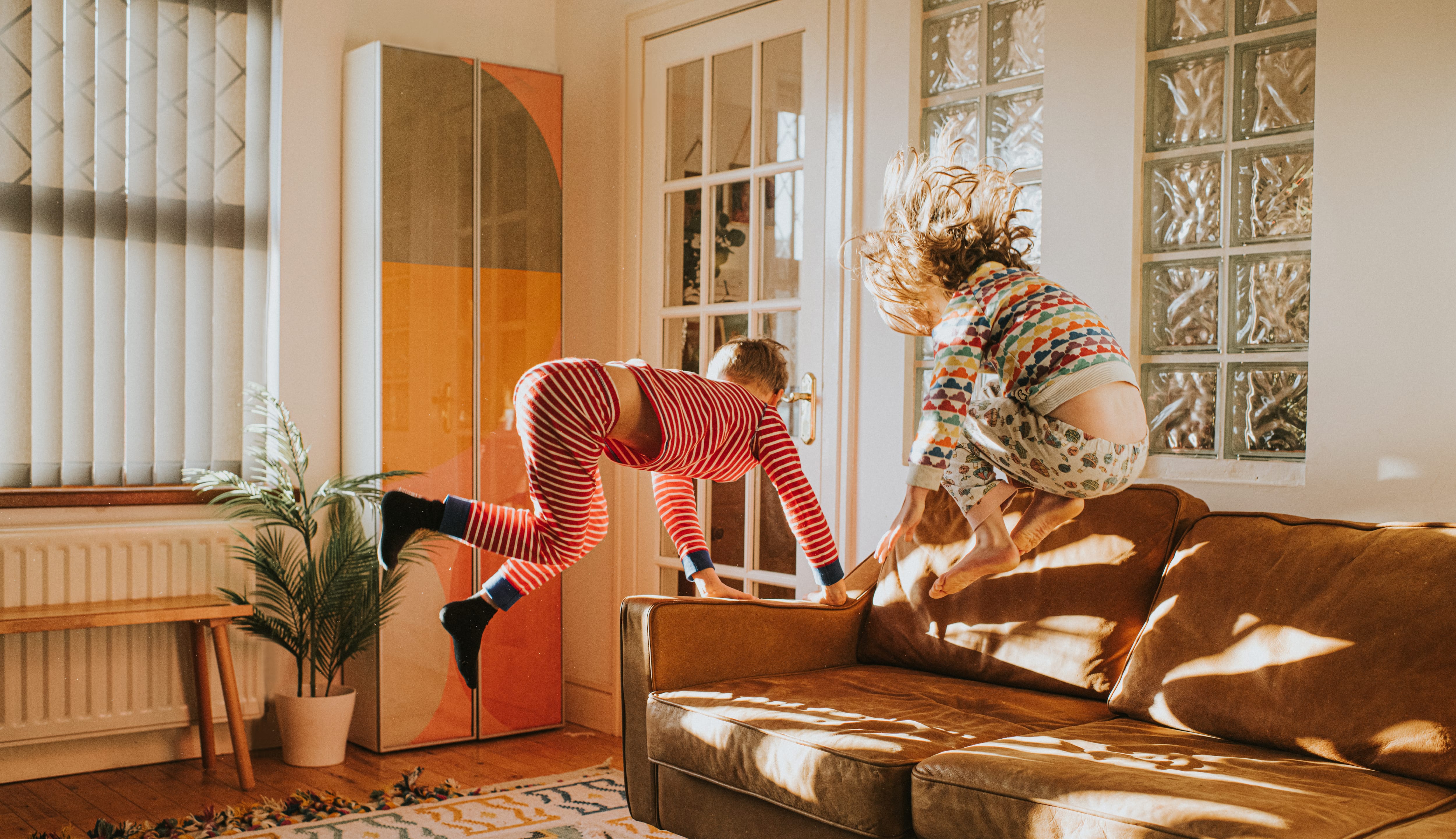 Kids jumping on brown leather couch in earth tone living room