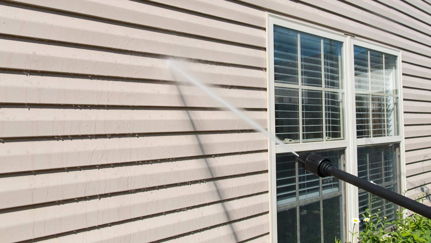 Close-up of pressure washing house’s siding
