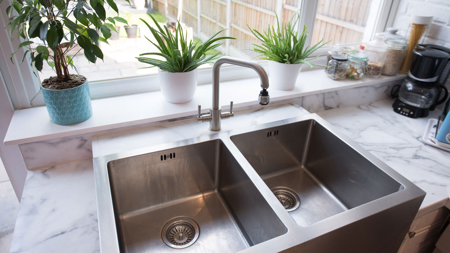 A stainless steel twin sink with marble countertop and view to the backyard