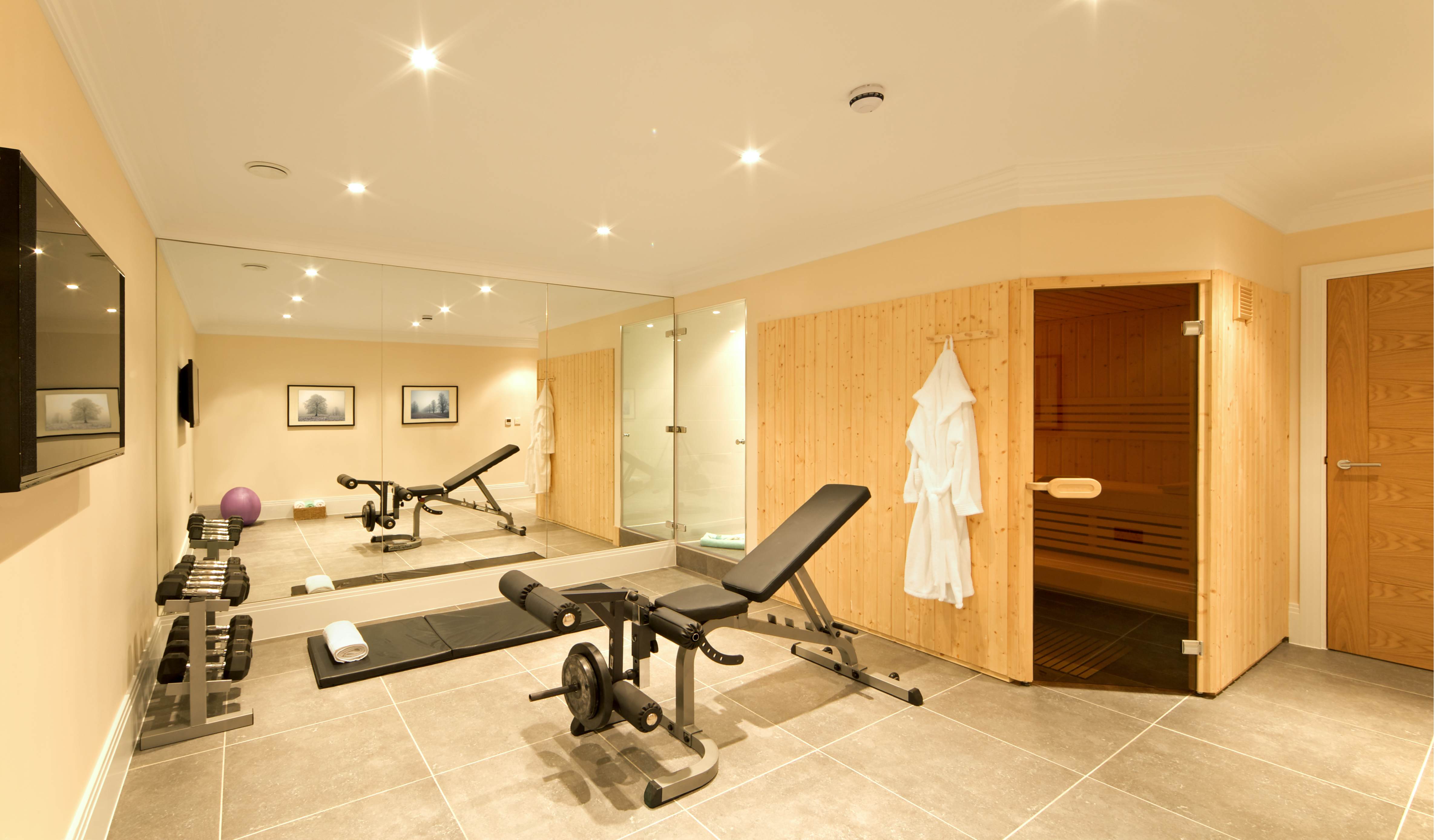 A basement home gym, fitted with exercise equipment including weights, a bench, ball and floor mat. A pine-panelled sauna and shower room are also part of the space.
