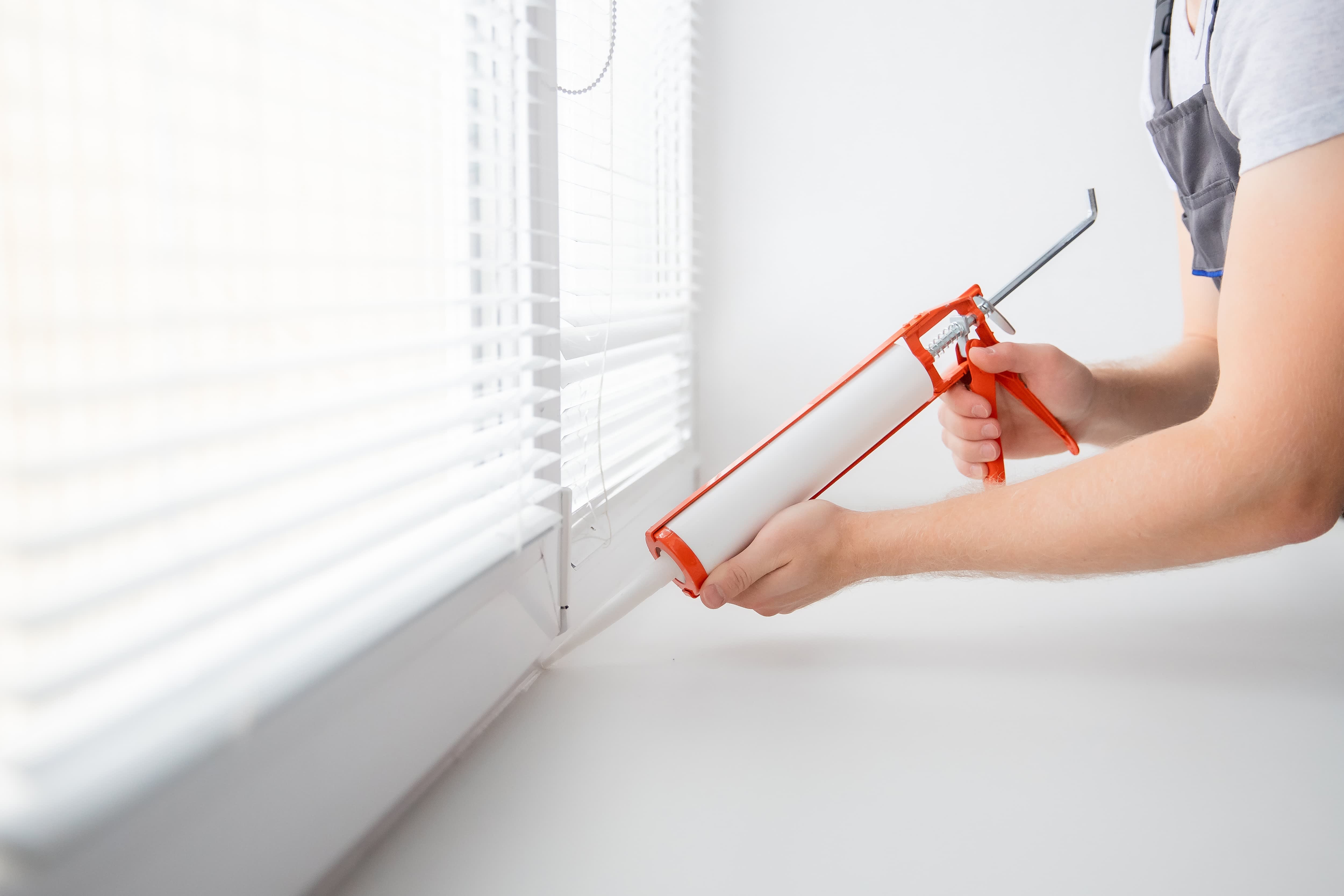 A person using a caulk gun to seal the edge around a window