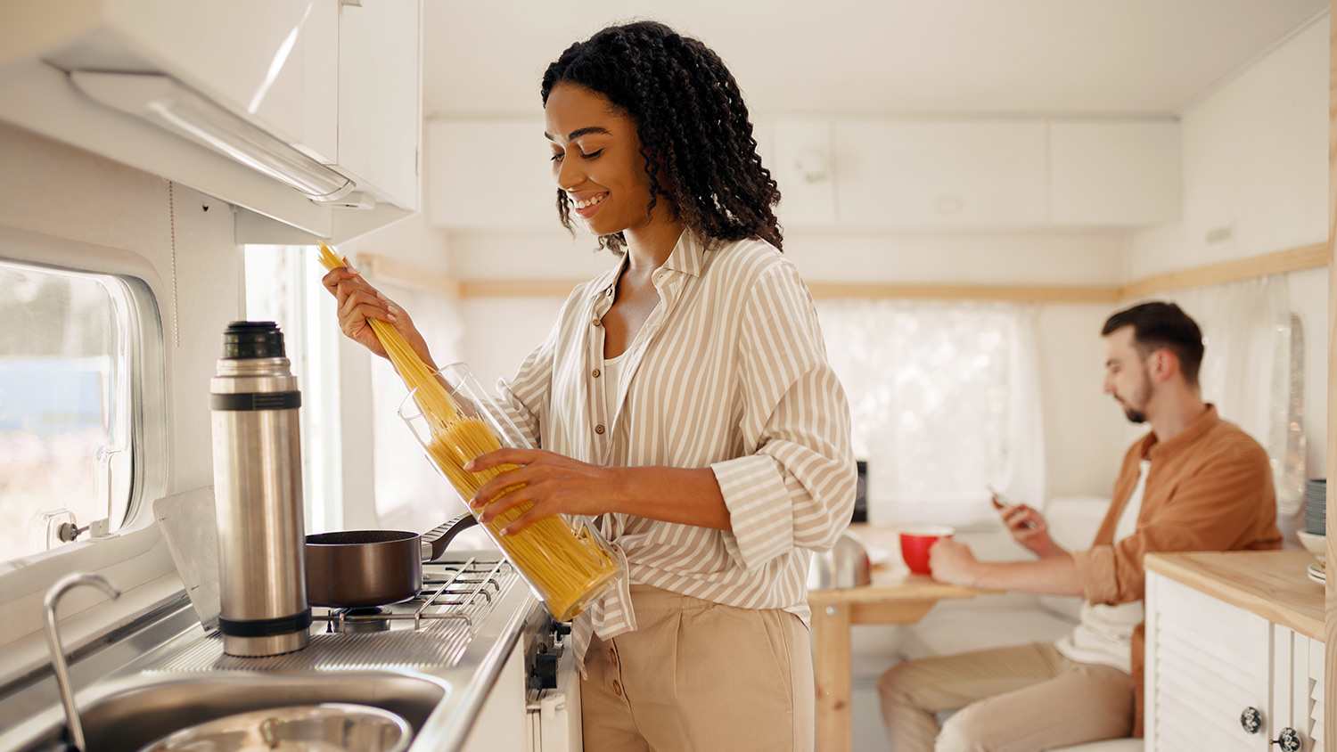woman making pasta and couple in tiny home having dinner