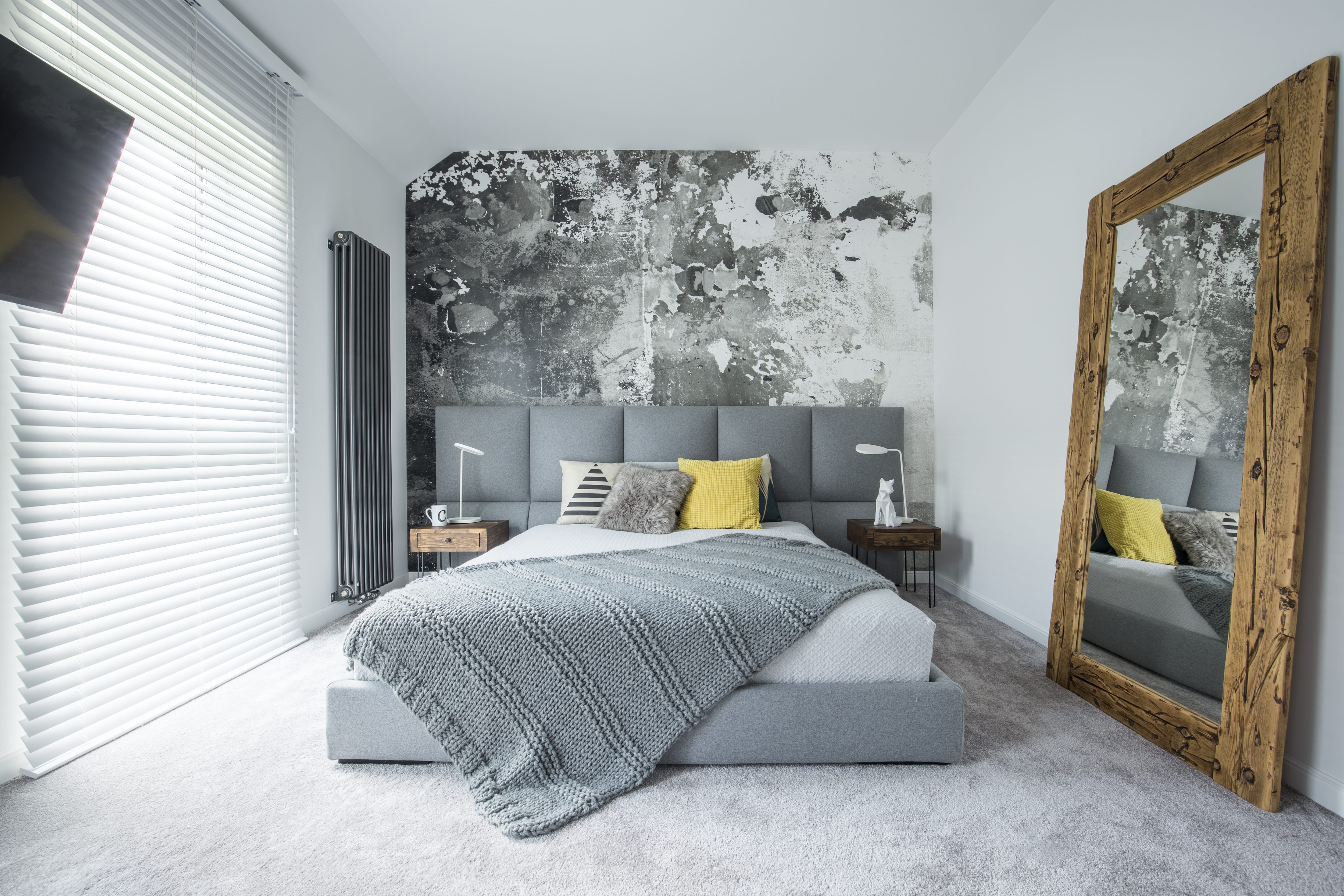 A small bedroom with gray accents and a large wood framed mirror