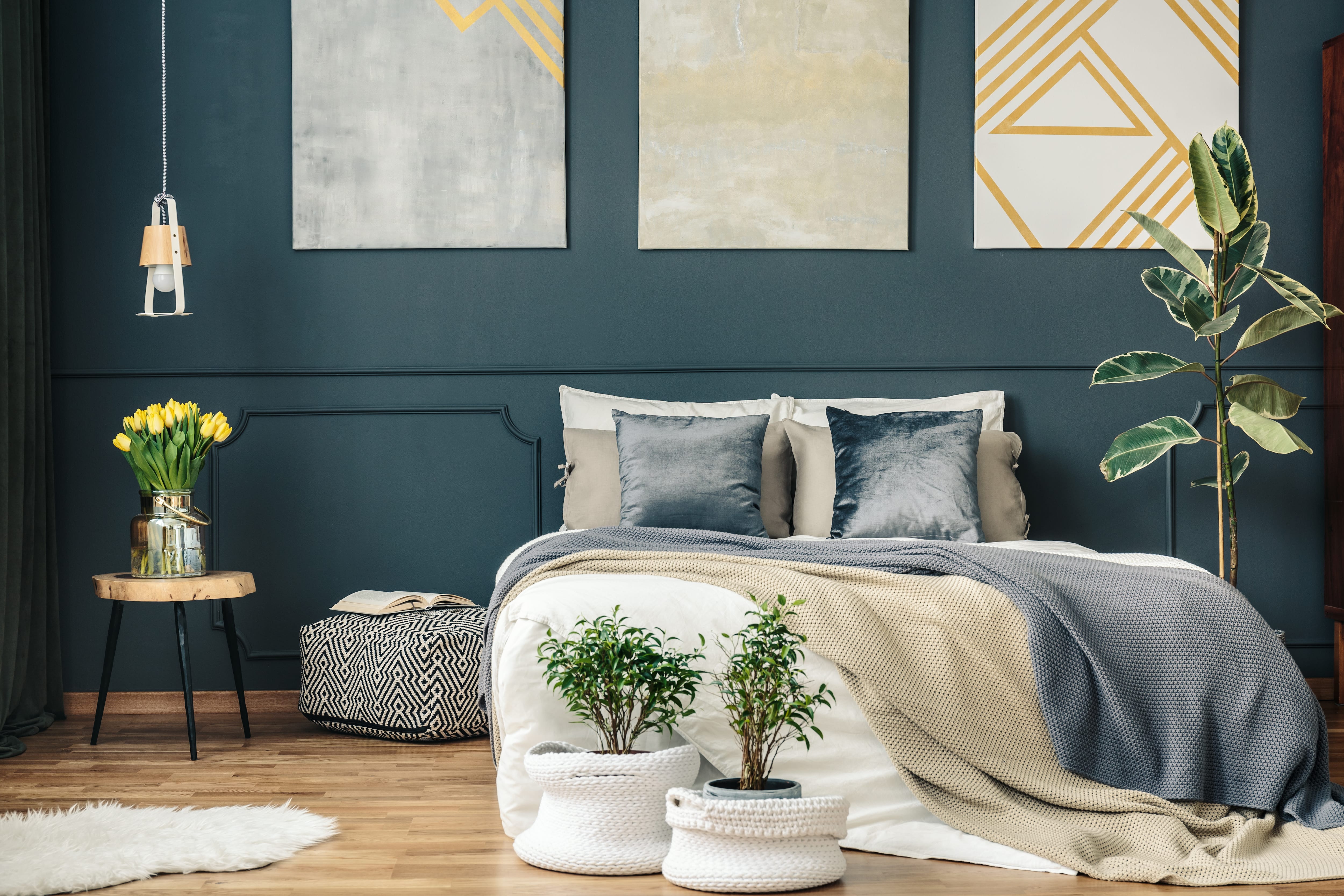 A bedroom with dark blue walls and natural wood accents and plants