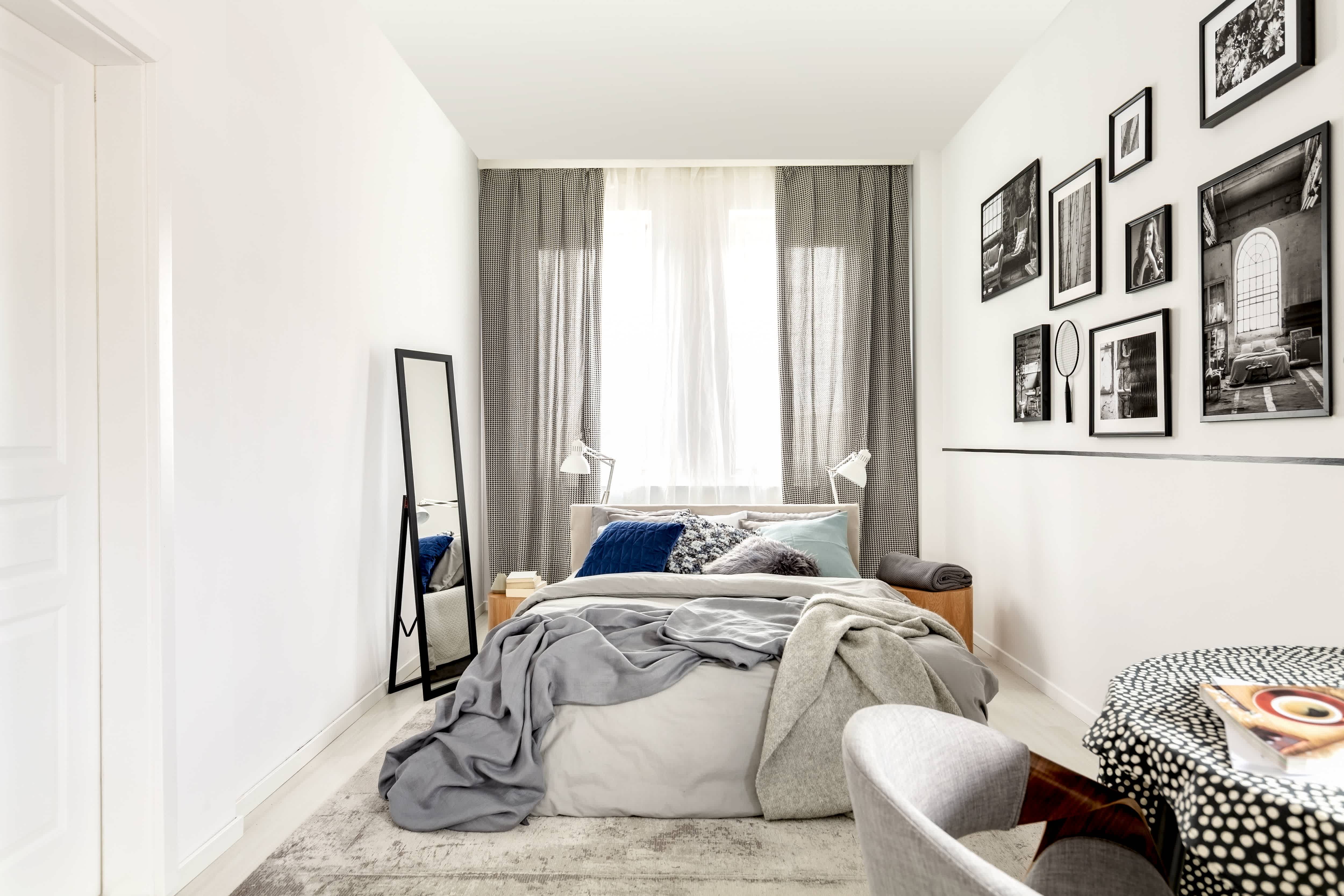 A small bedroom with high curtains and a mirror
