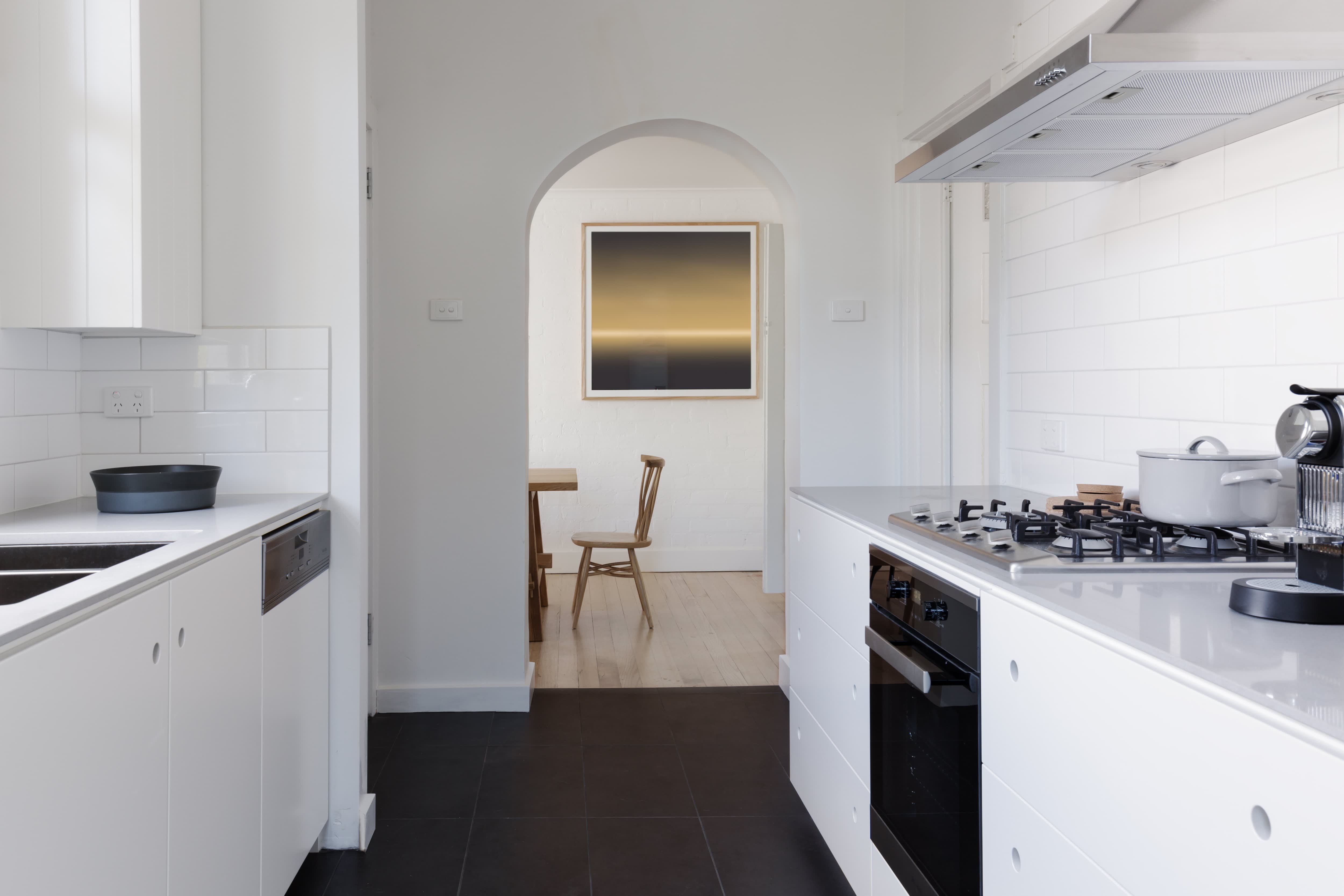 A modern white galley kitchen with black appliances and dark floors