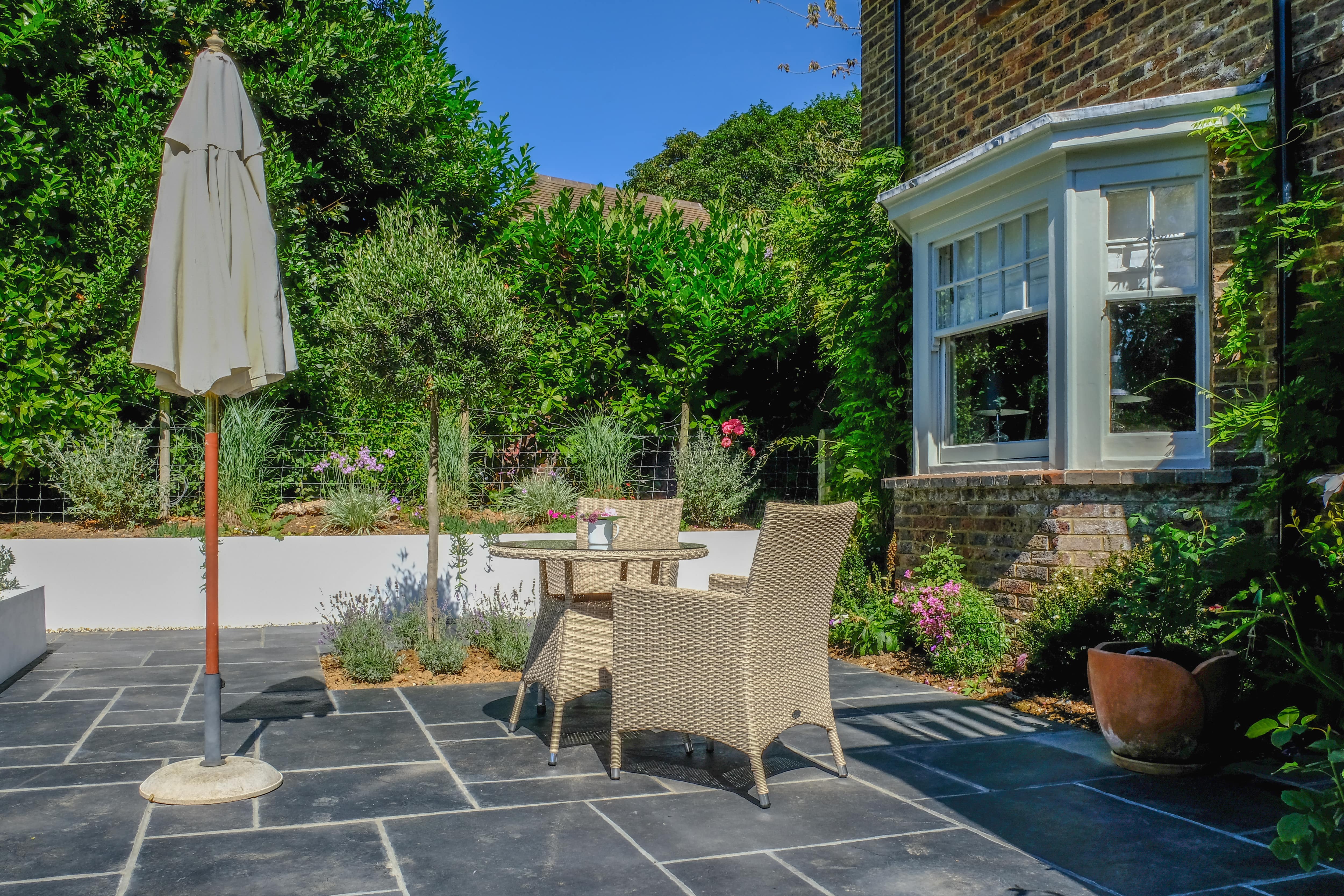A backyard bluestone patio with an umbrella and wicker patio set