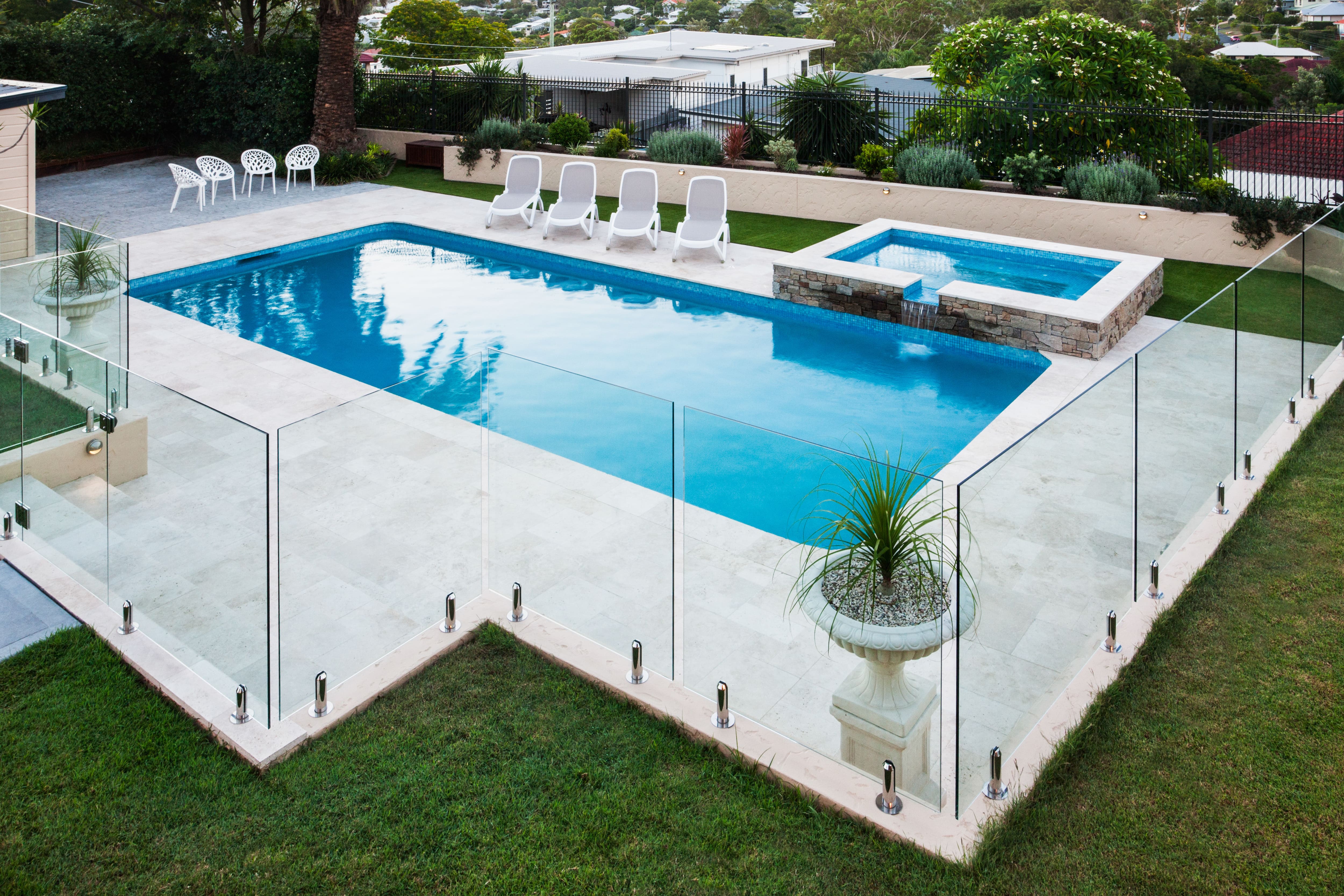 An inground pool with a glass wall fence installed around the patio edge