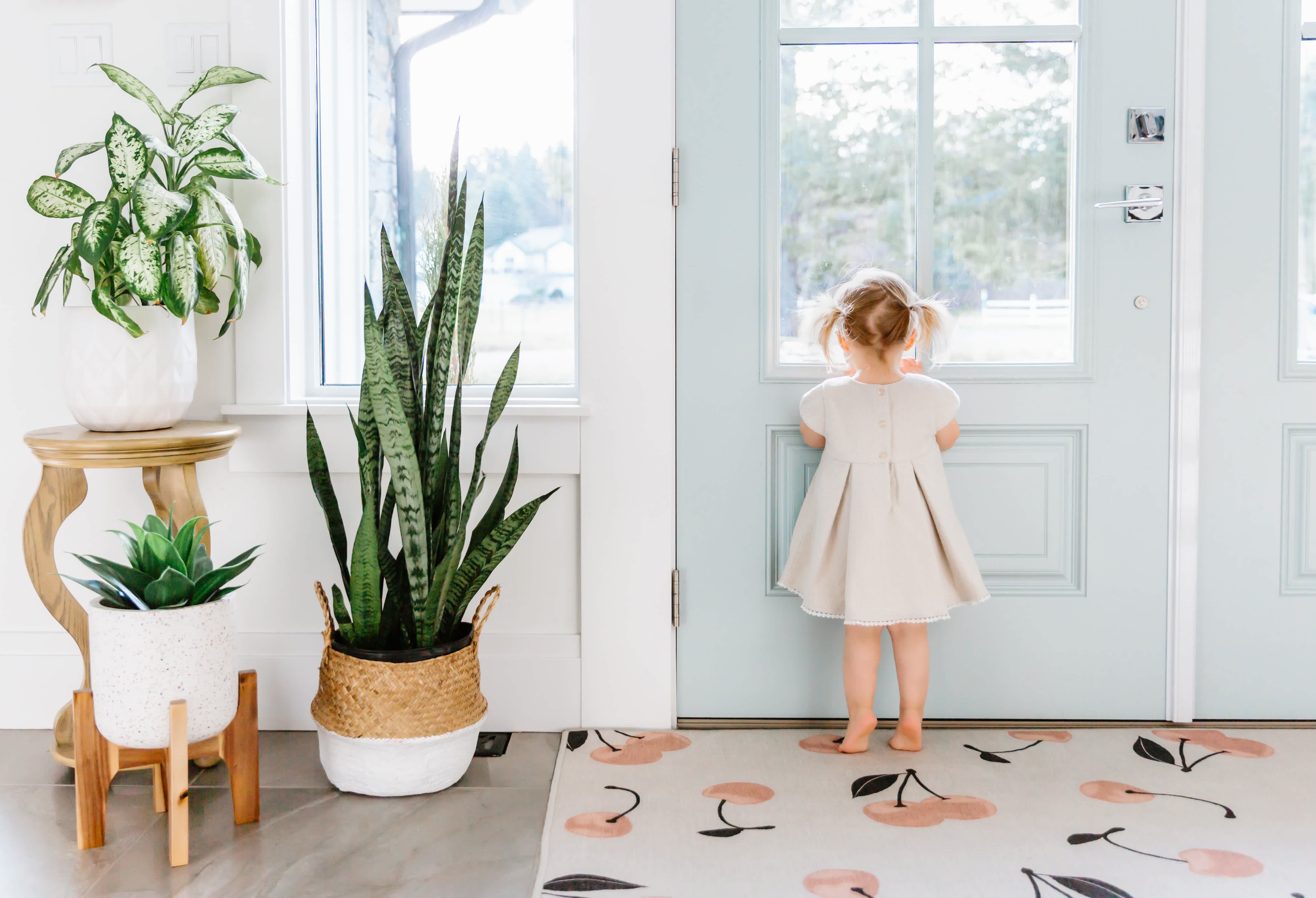 A little girl standing on a cherry print rug at the front door