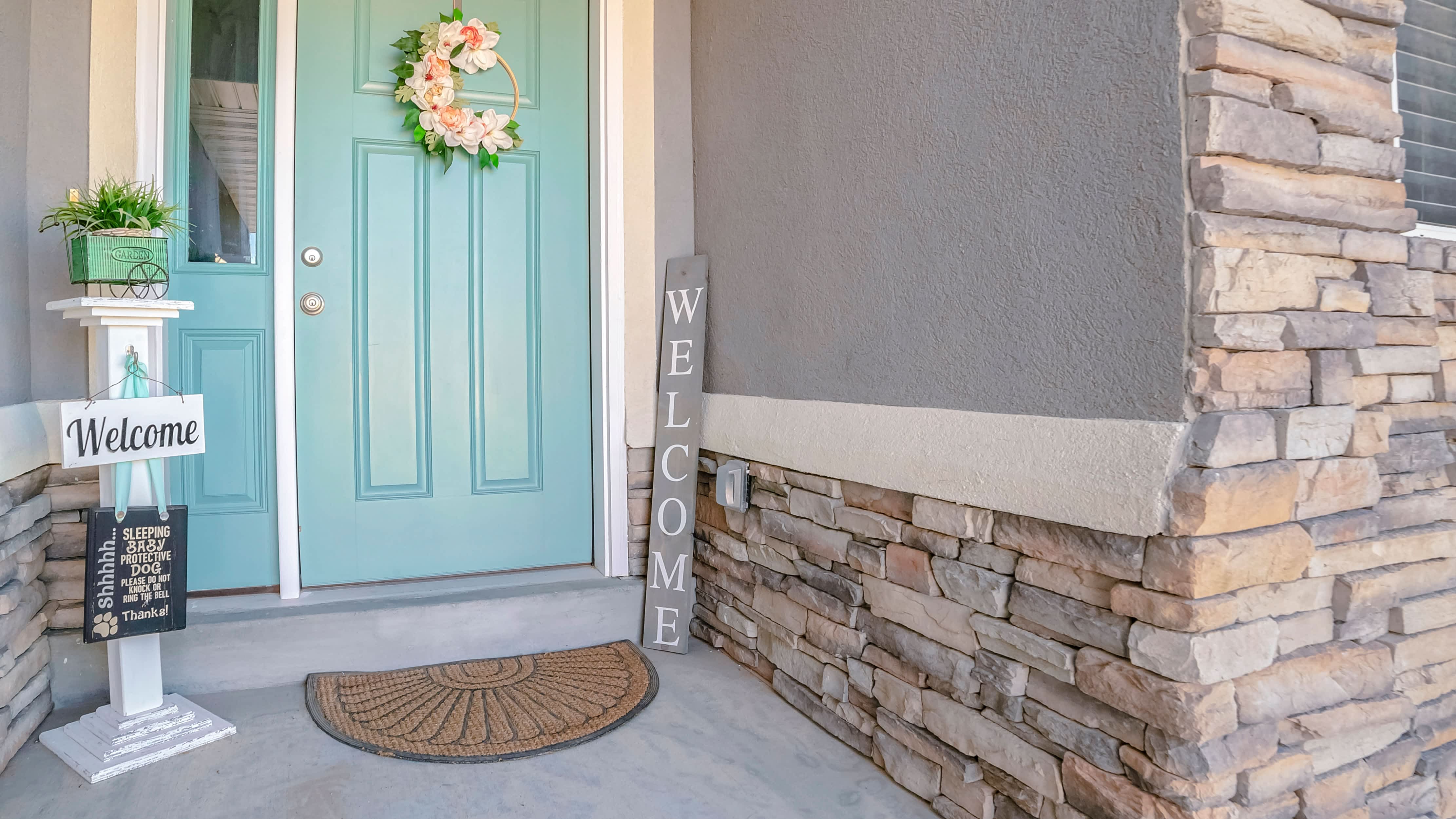A residential exterior with a blue door, decorative signs, a doormat, and flower wreath
