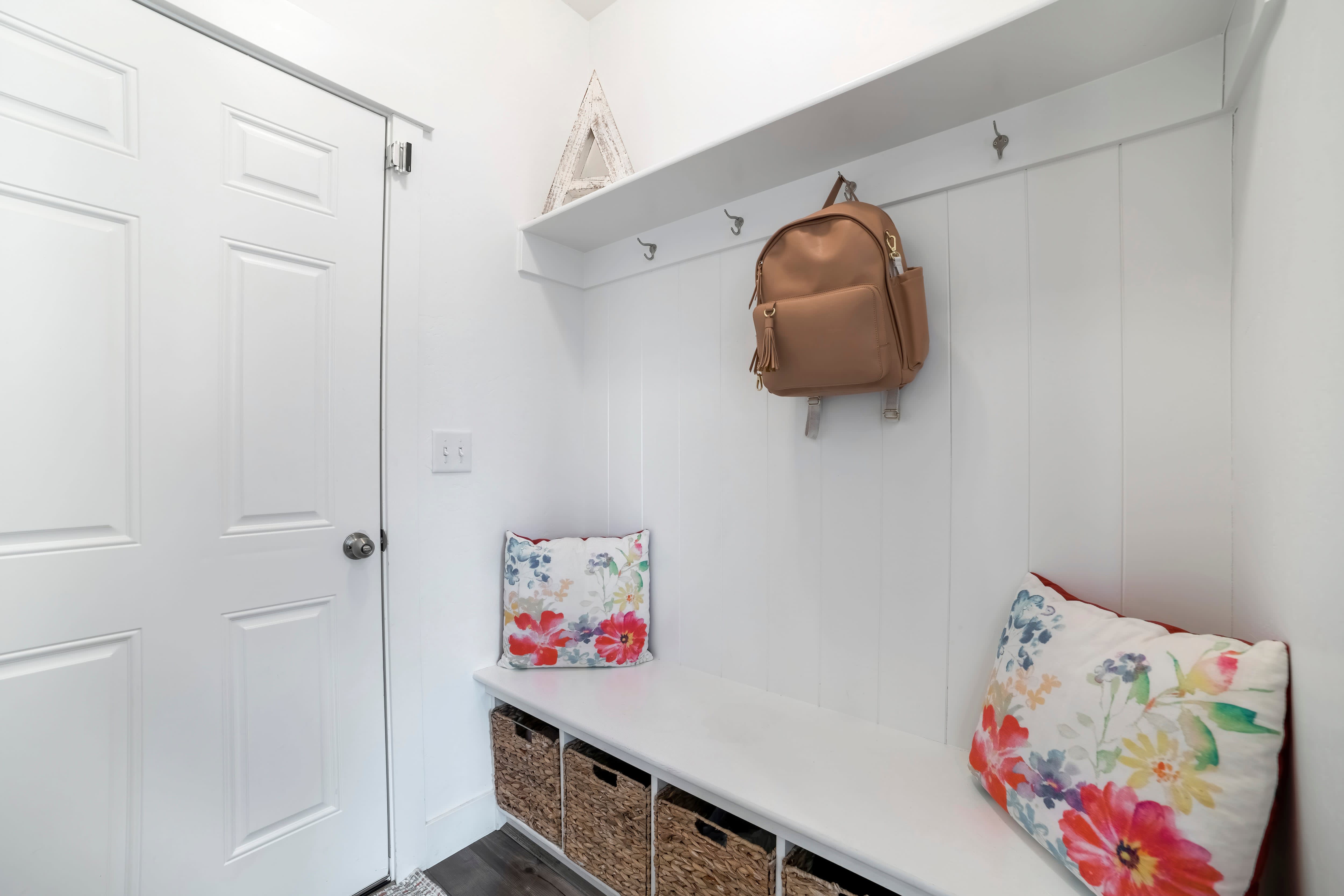 An all-white mudroom with a shelf, bench, storage baskets, and coat hooks