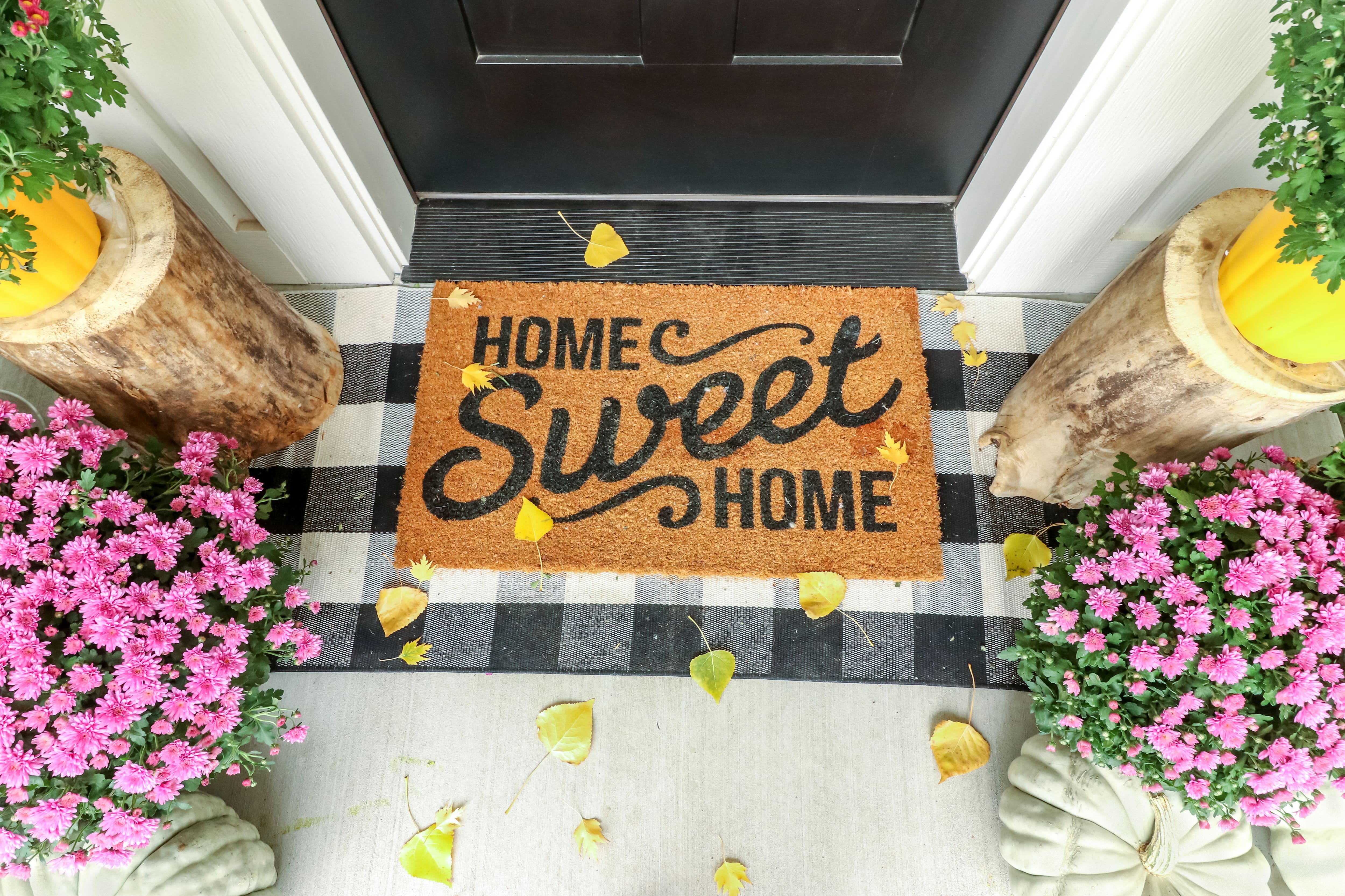 A front door decorated with bright flowers and a doormat that says “home sweet home”