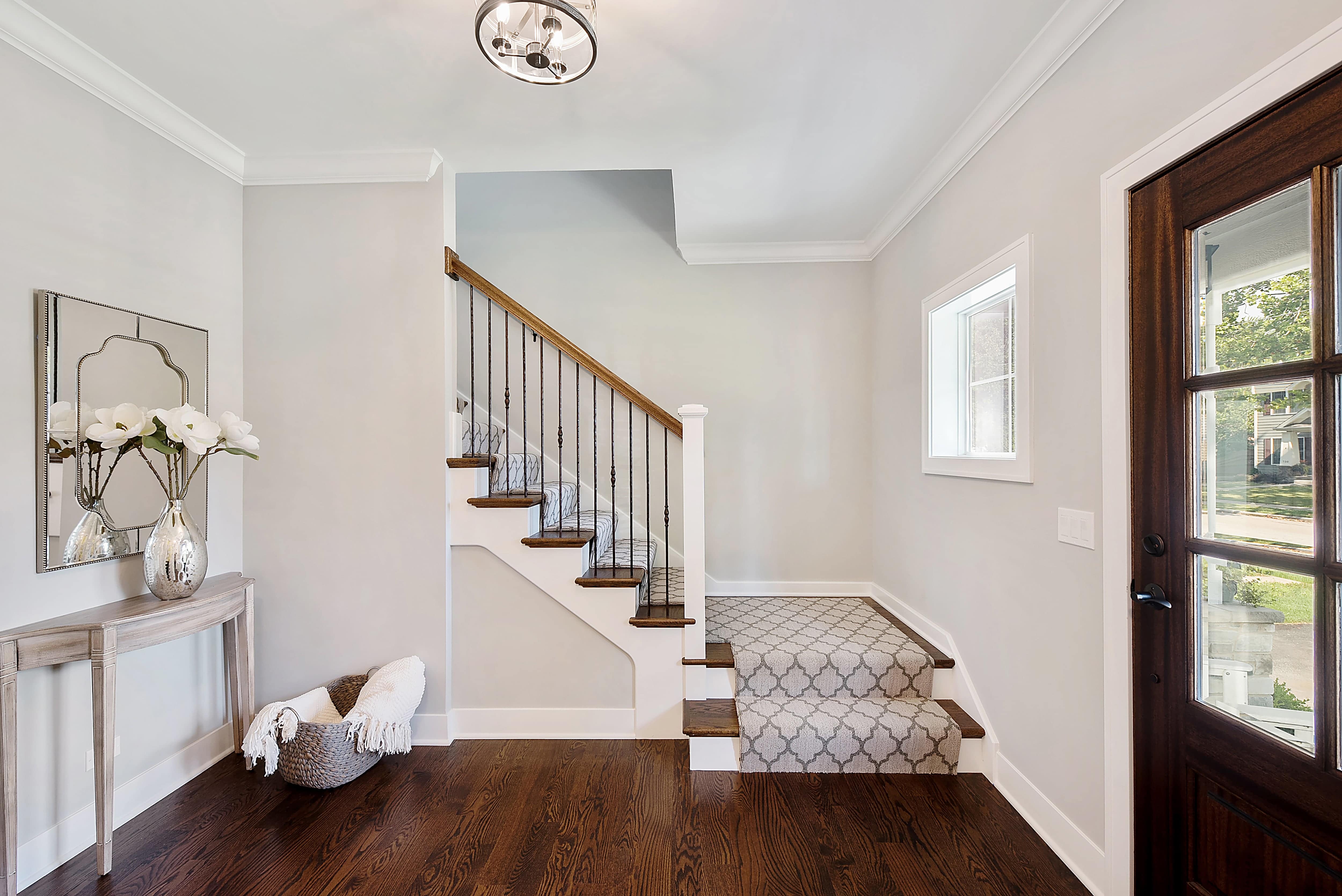 A bright, neutral entryway with a side table, large flower vase, and decorative mirror