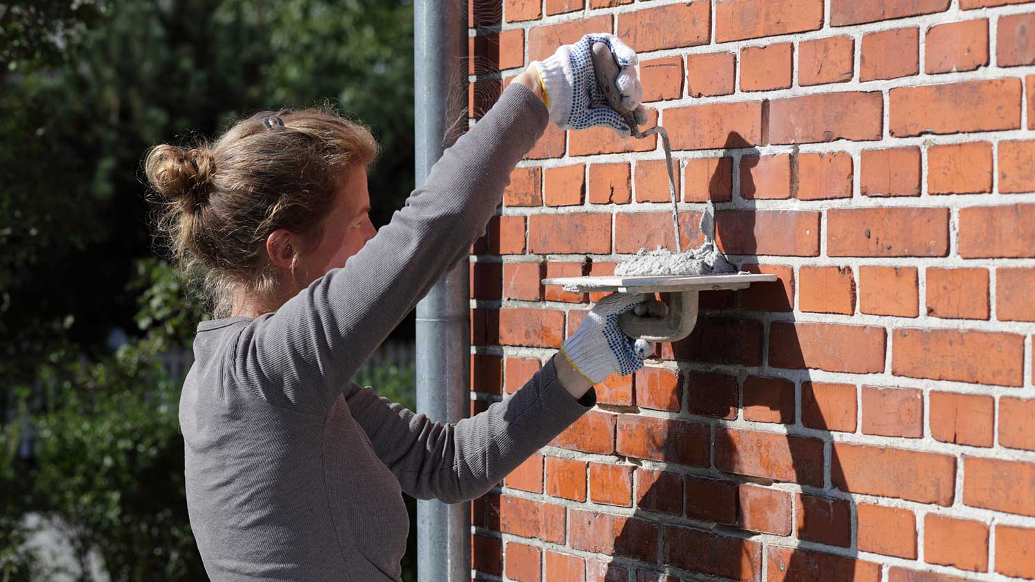 Woman repairing mortar on an exterior brick wall