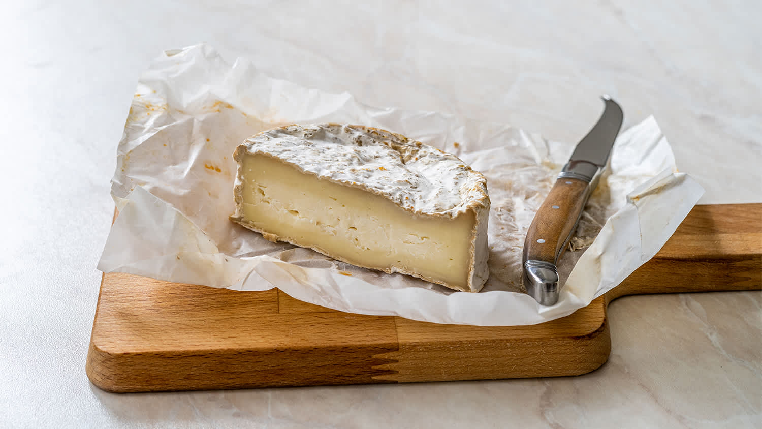brie cheese wrapped in wax paper on cutting board