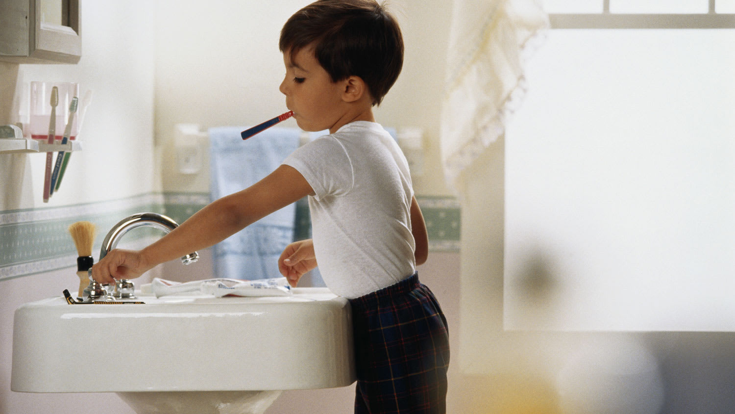 Boy with toothbrush in mouth turning off the tap
