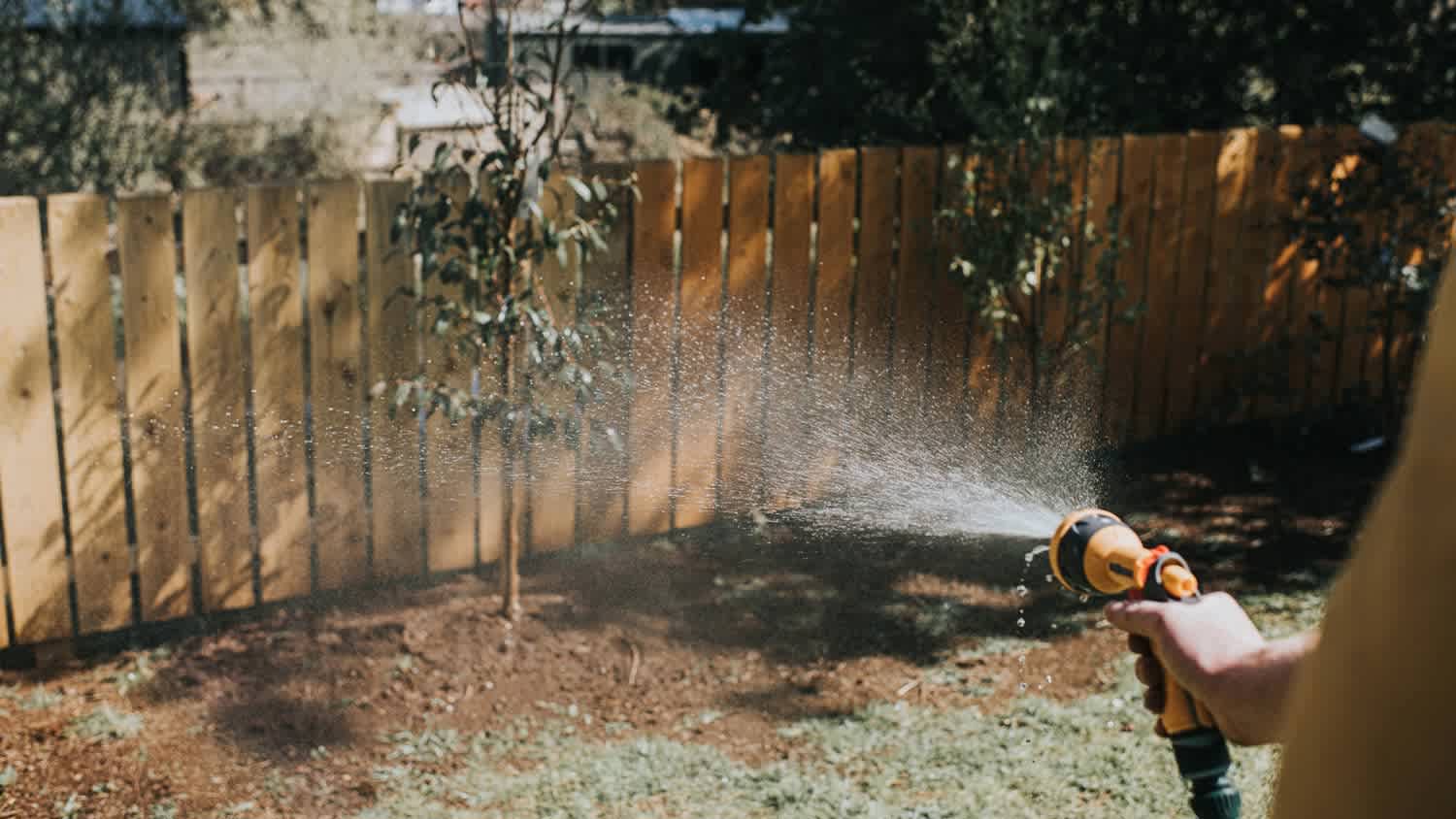 A man hosing a wooden fence in the backyard