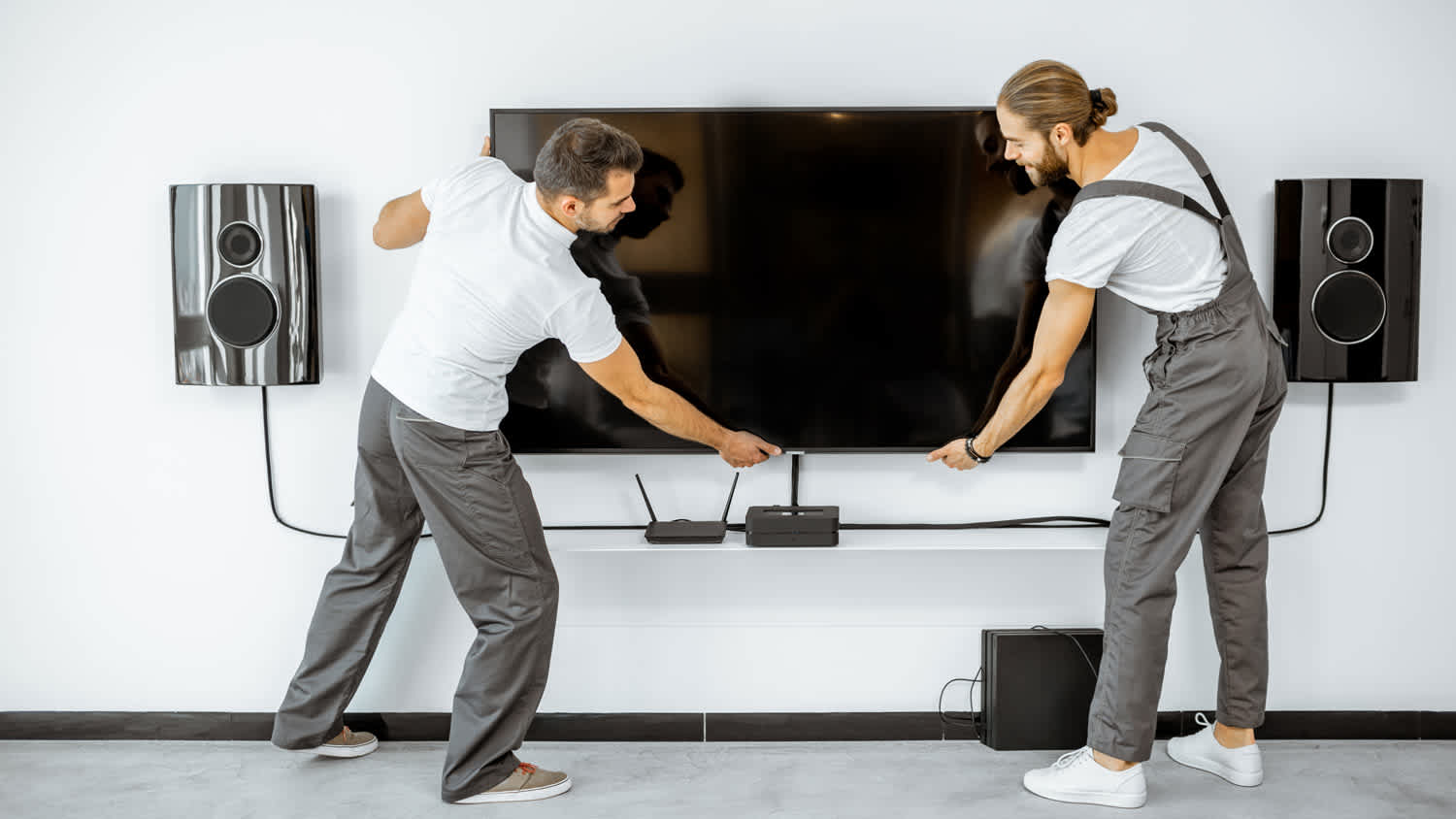 Two professionals installing a large TV and audio system