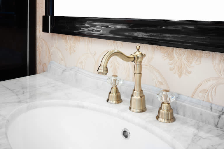 closeup of gold bathroom faucet on marble countertop with white sink